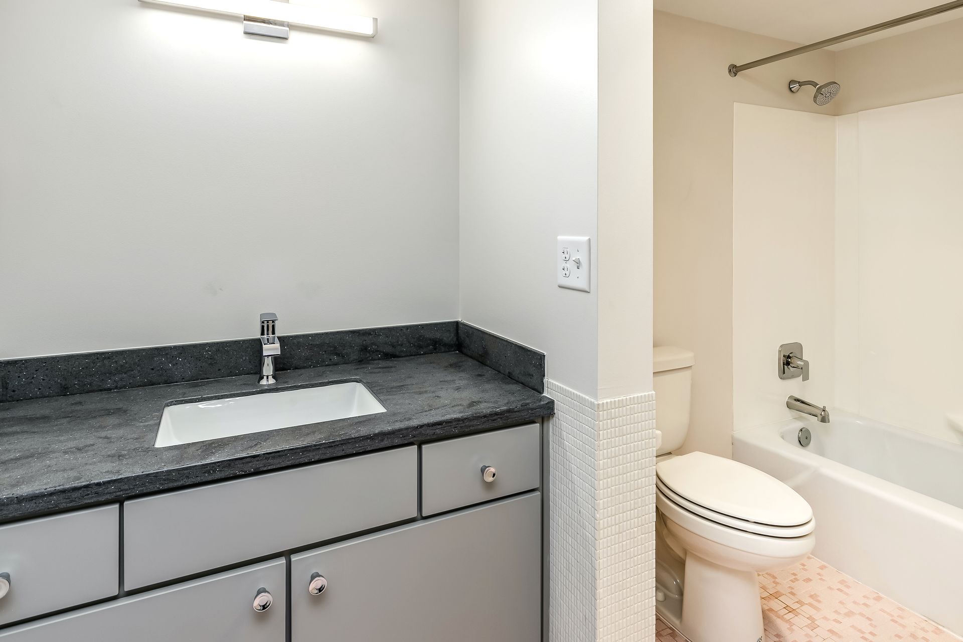 Bathroom vanity with dark countertop and sink beside a toilet in a small beige restroom