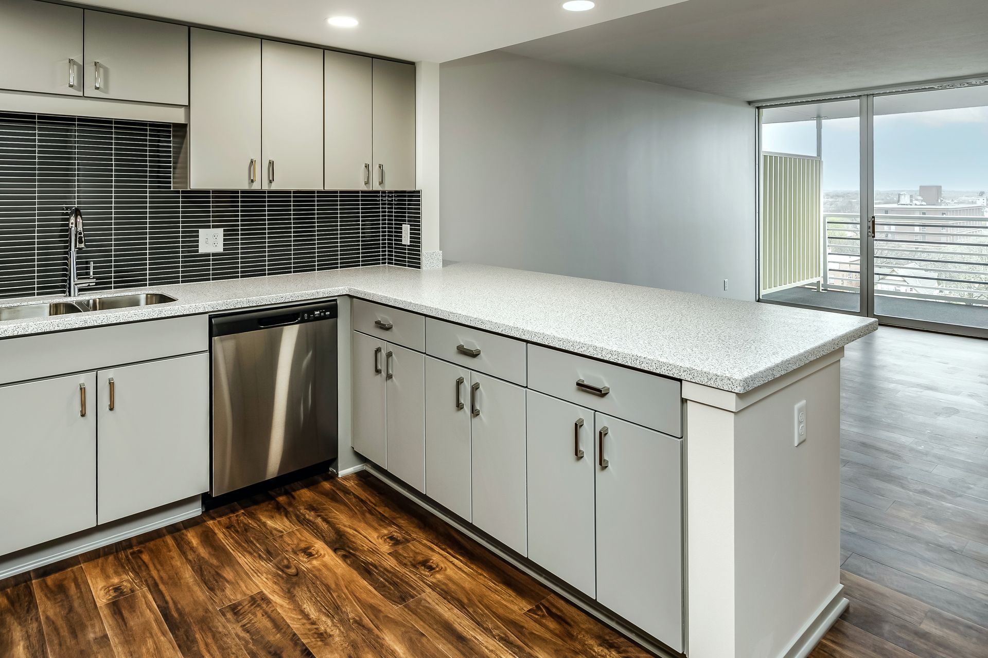 Bright modern kitchen with white cabinets, gray countertops, wood floors, and a large island by sliding doors
