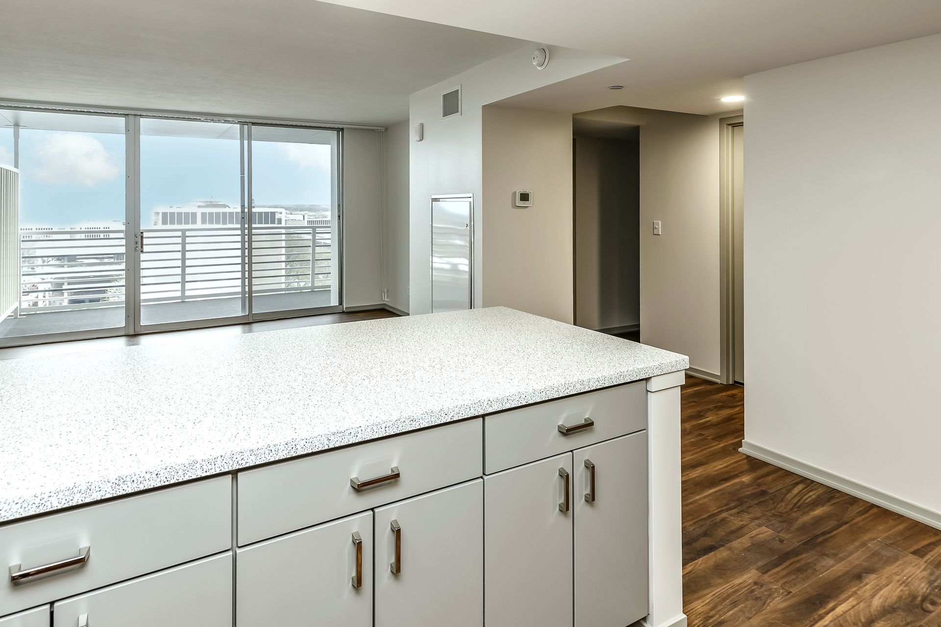 Bright kitchen with white cabinets, stone island, wood floor, and large windows overlooking a city view