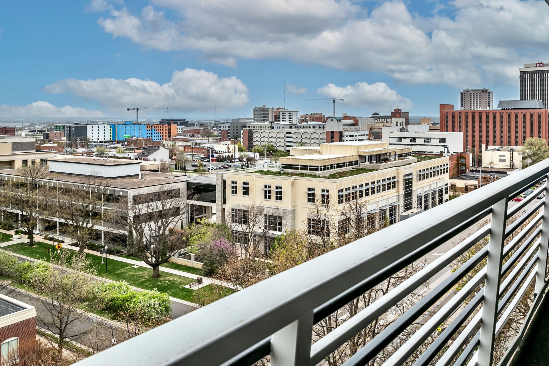 City skyline and buildings seen from a balcony with a metal railing under a partly cloudy sky
