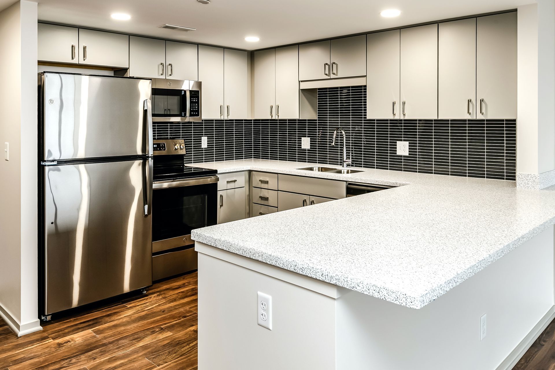 Modern kitchen with stainless steel appliances, white cabinets, black backsplash, and large island countertop