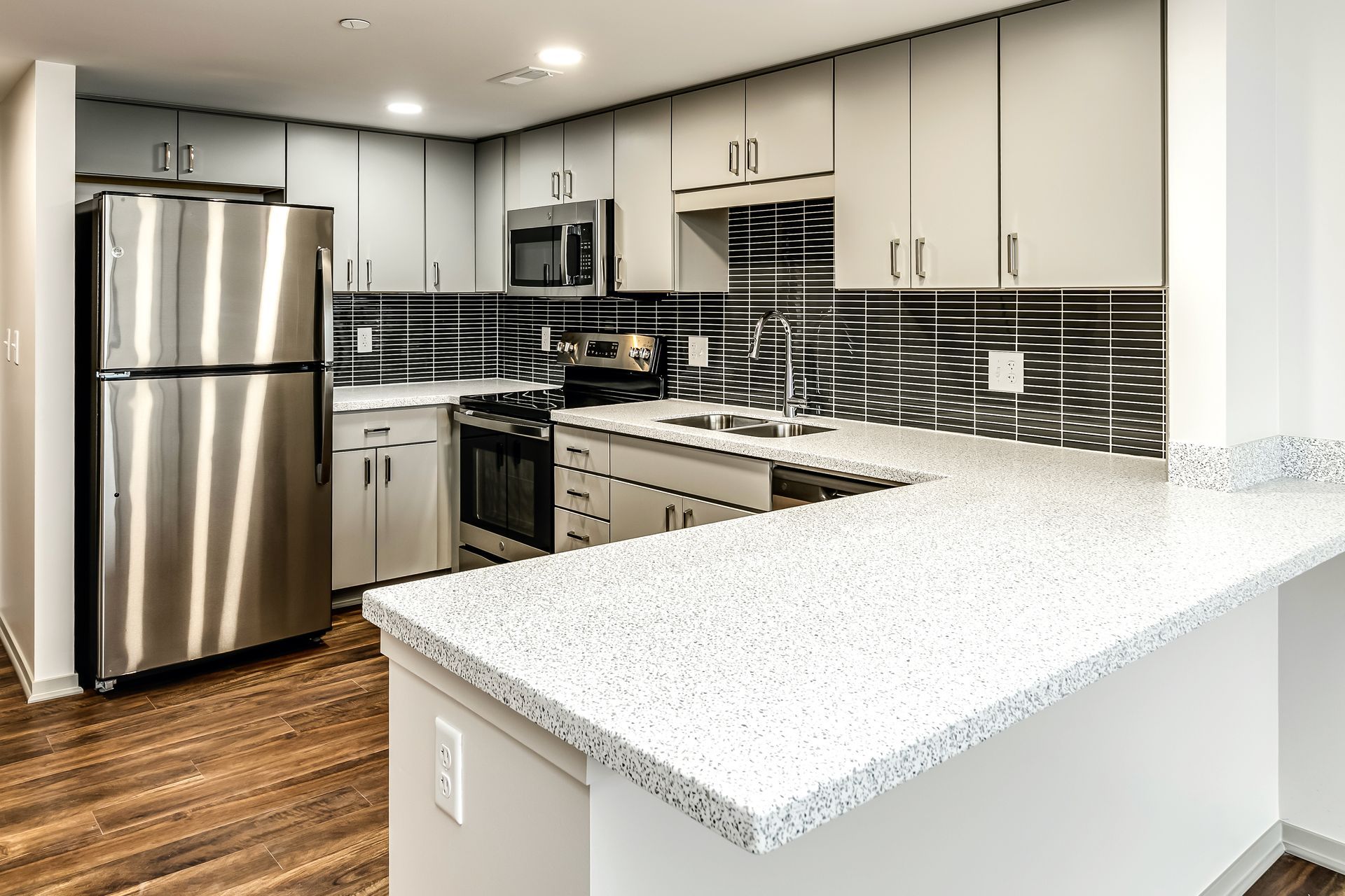 Modern kitchen with stainless steel appliances, white cabinets, dark tile backsplash, and a light granite island.