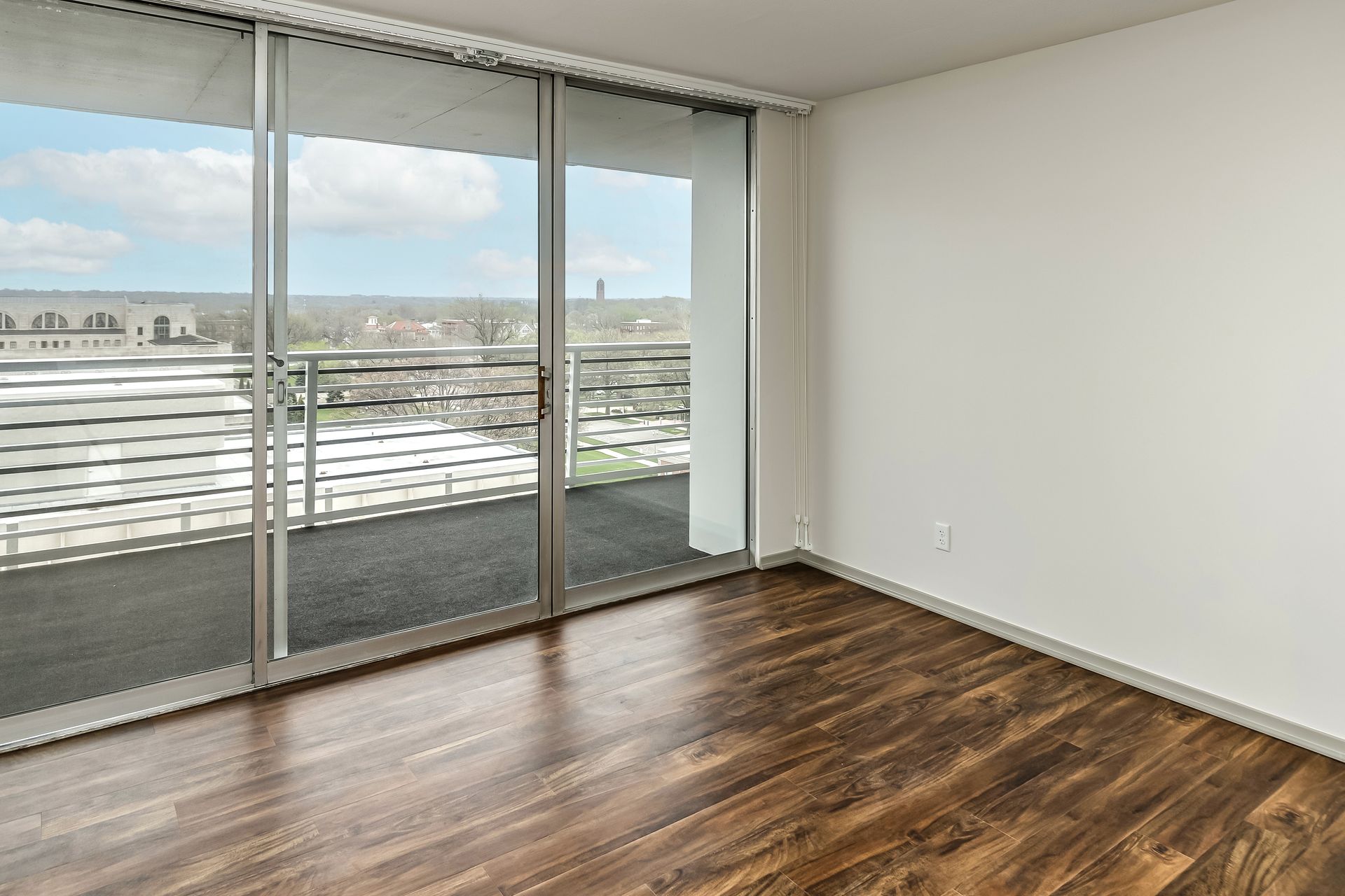 Empty room with wood floors and a sliding glass door opening to a balcony with a city view