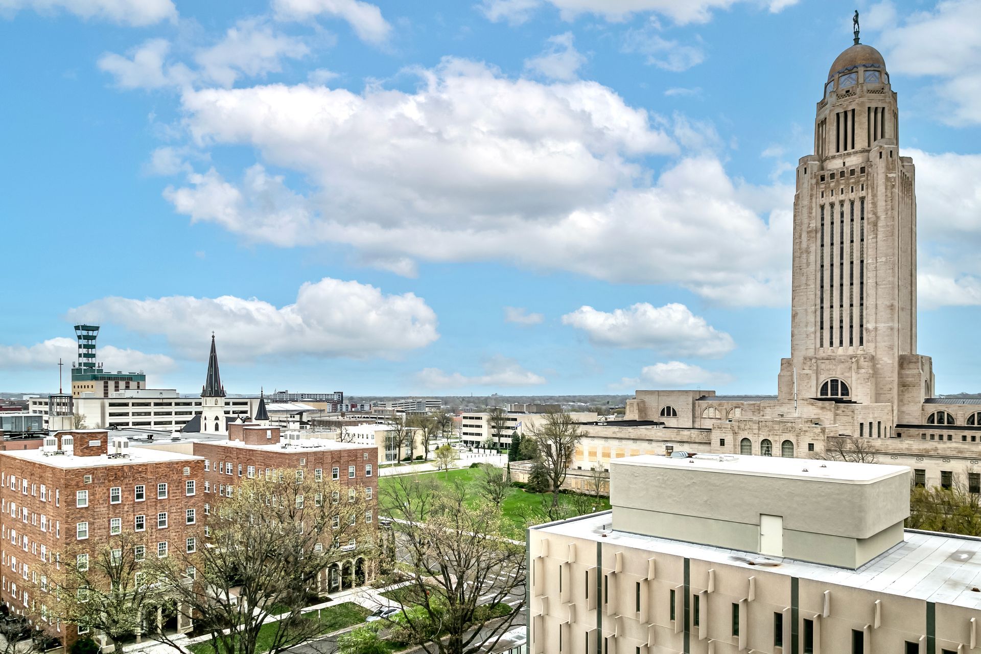 City skyline with a tall stone tower under a bright blue sky with clouds