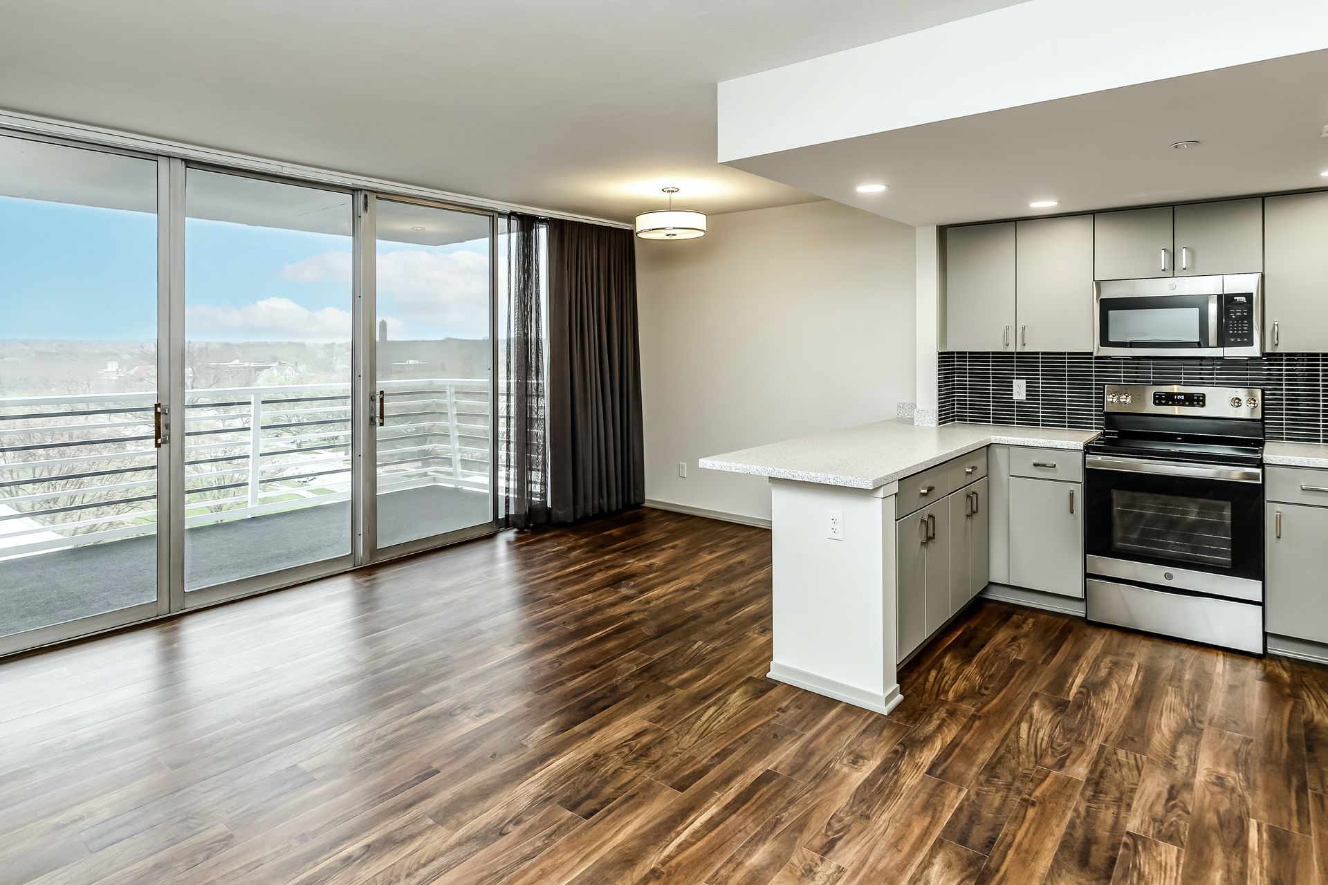 Empty modern apartment interior with wood floors, kitchen island, and floor-to-ceiling windows with city view