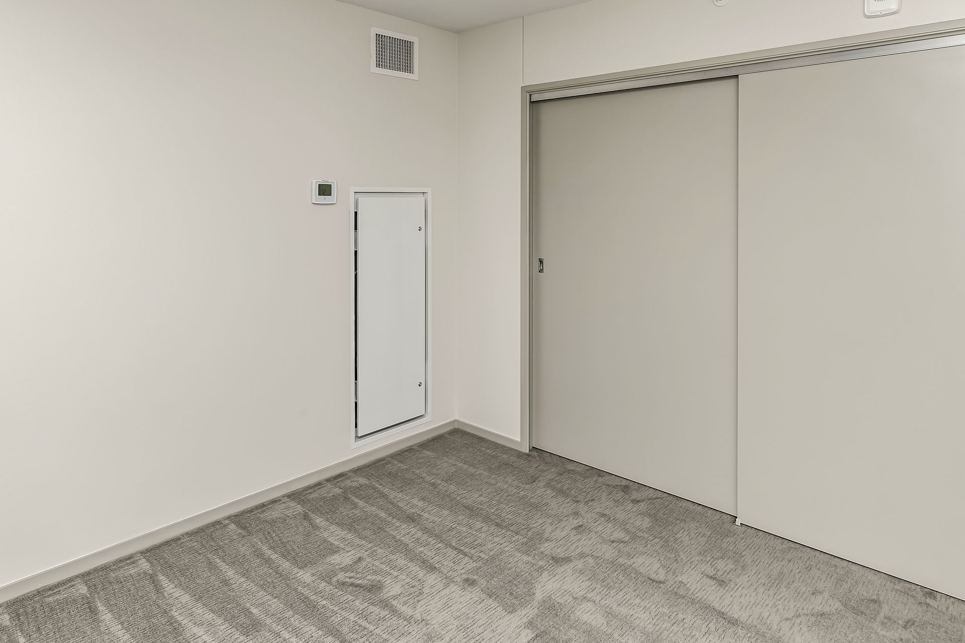 Empty carpeted room with white walls, a closet, and a small wall access panel.