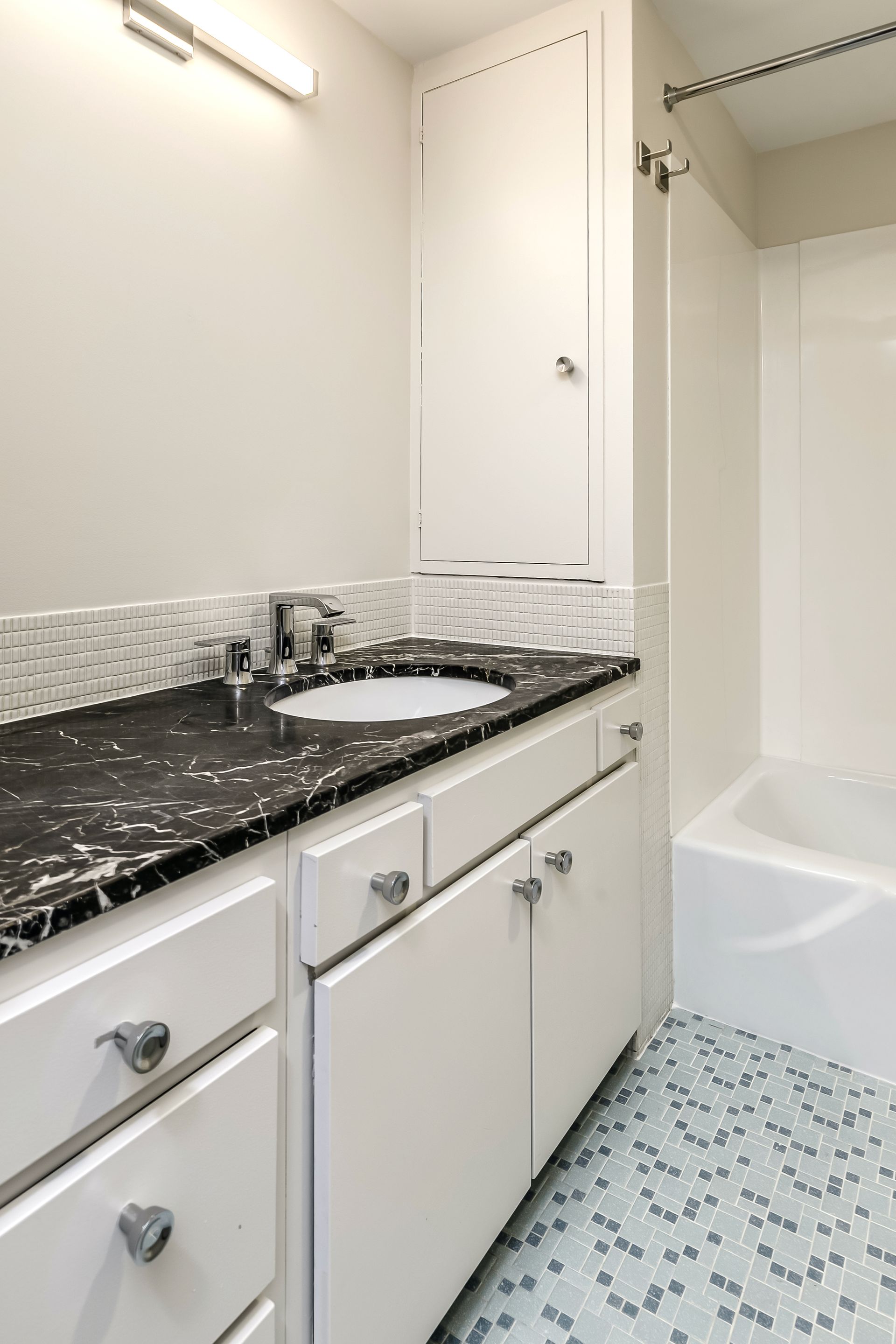 Bathroom vanity with black countertop, white cabinets, and tiled floor beside a bathtub.