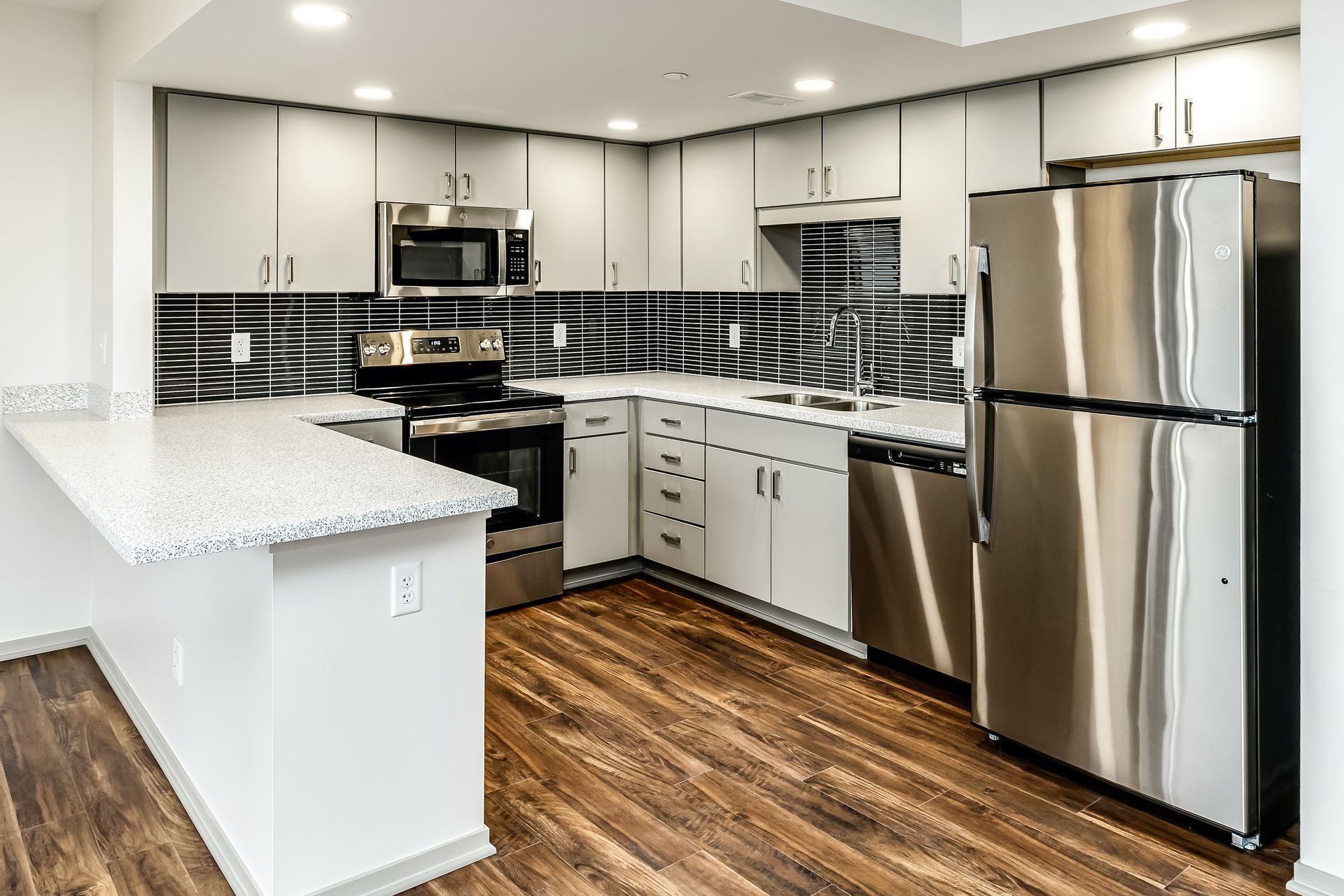 Modern kitchen with stainless steel appliances, white cabinets, black backsplash, and wood flooring