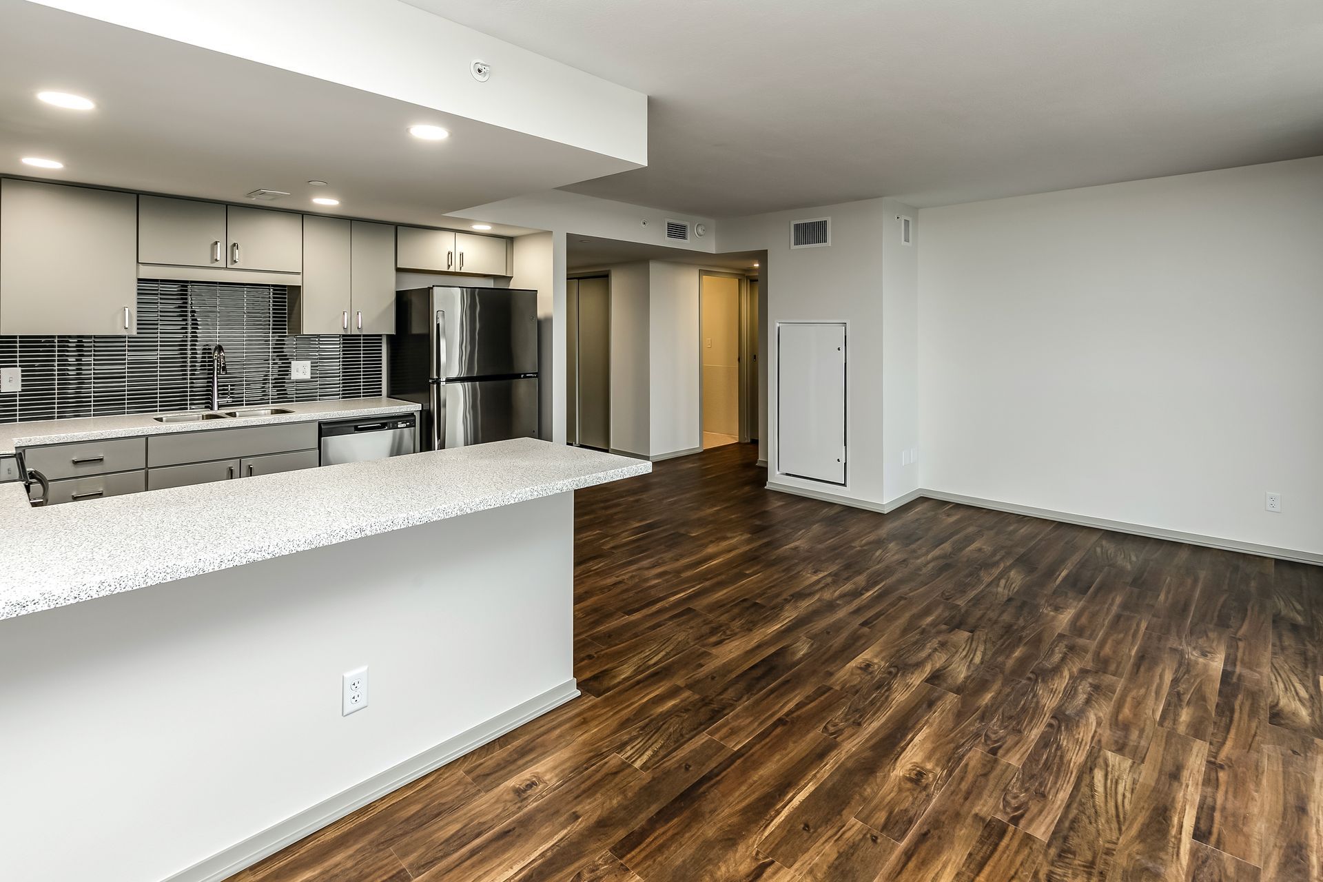 Empty modern apartment kitchen and living area with granite counter, stainless appliances, and wood floors