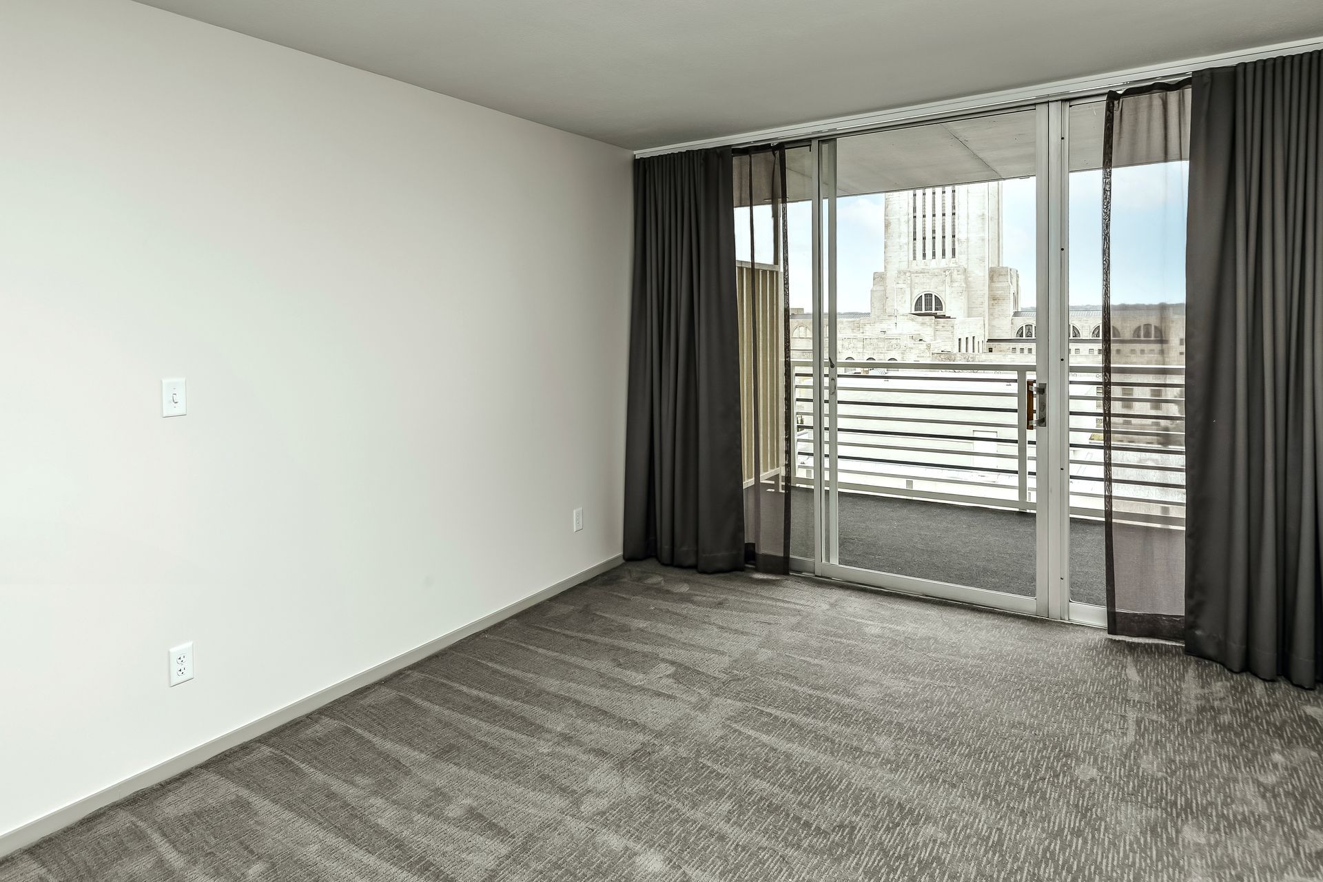 Empty carpeted living room with sliding glass doors opening to a balcony and city view