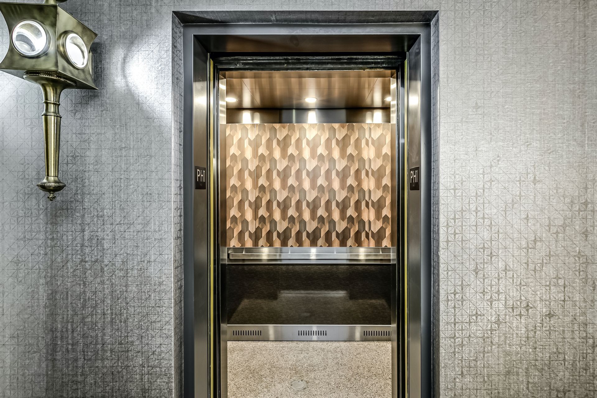 Closed elevator doors with a gold patterned panel inside a textured gray hallway