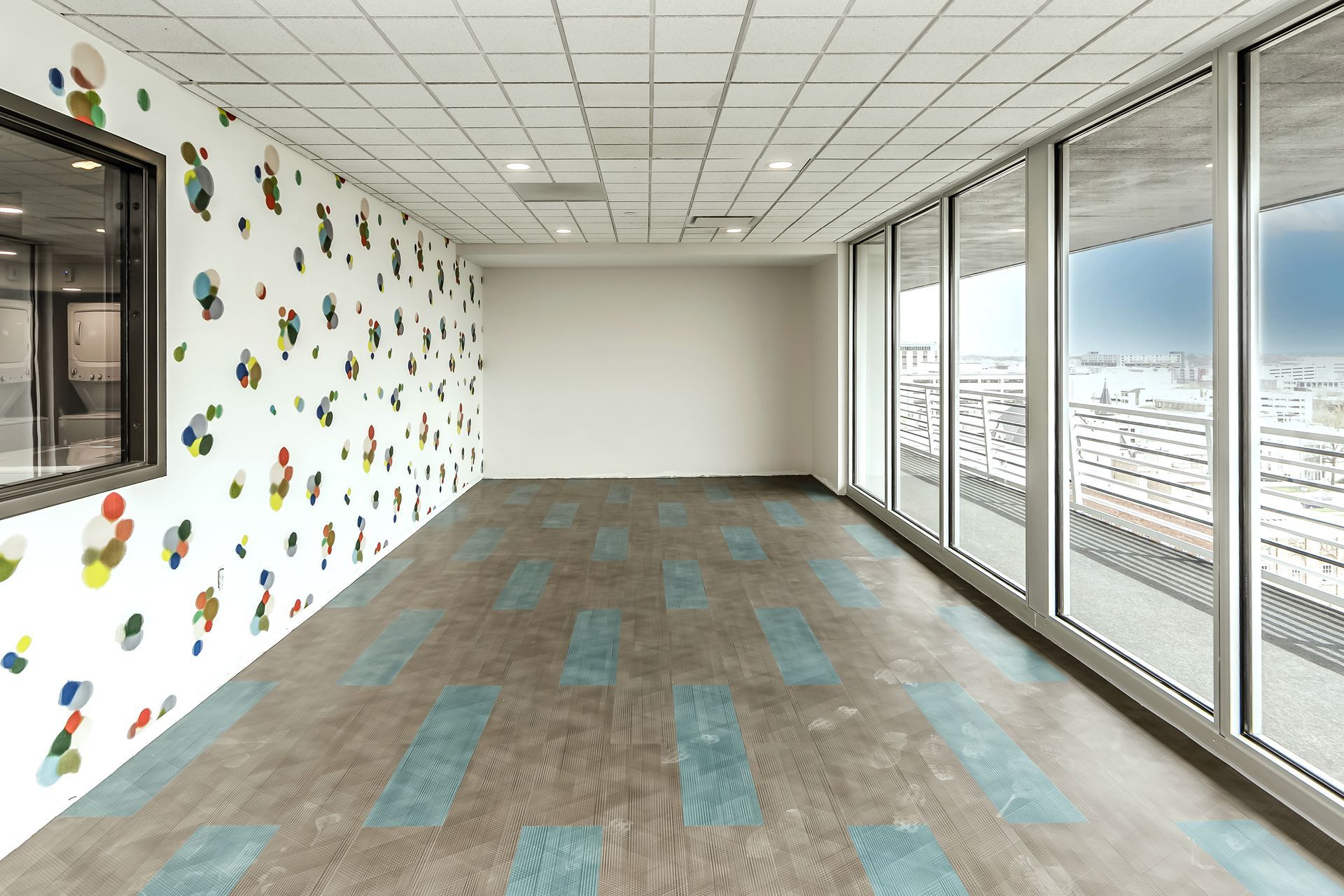 Empty office room with patterned wall, carpeted floor, and large windows overlooking snowy cityscape.