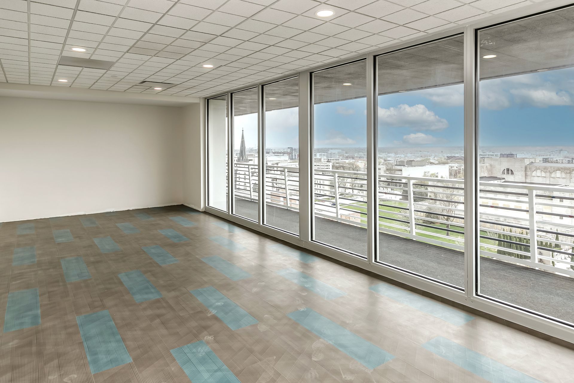 Empty modern office with large windows, city view, and gray-blue carpet tiles