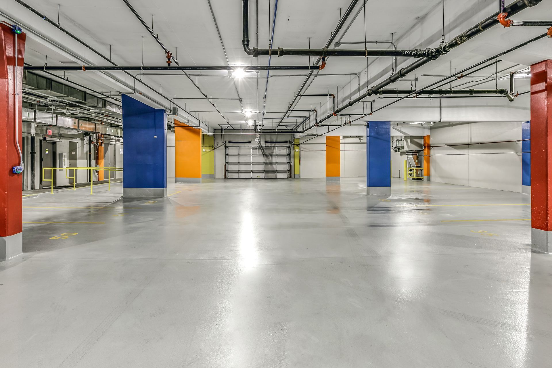 Empty industrial warehouse with polished concrete floor, exposed pipes, and blue and orange columns