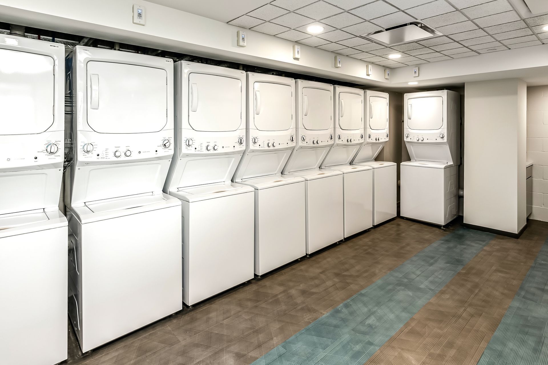 Laundry room with stacked white washers and dryers along the wall under fluorescent lights