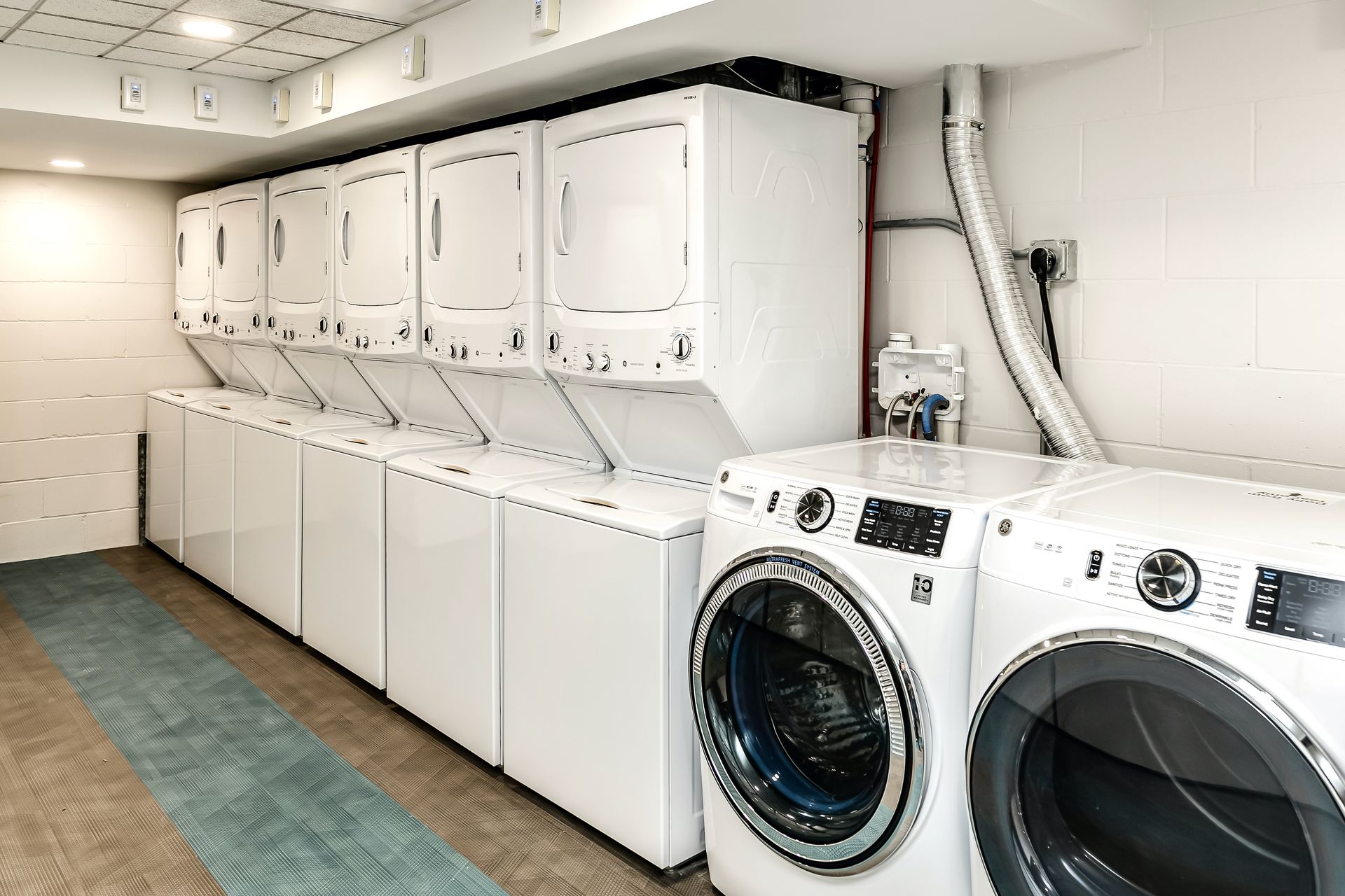 Laundry room with stacked washers and dryers along a wall, plus two front-loading machines in the foreground.