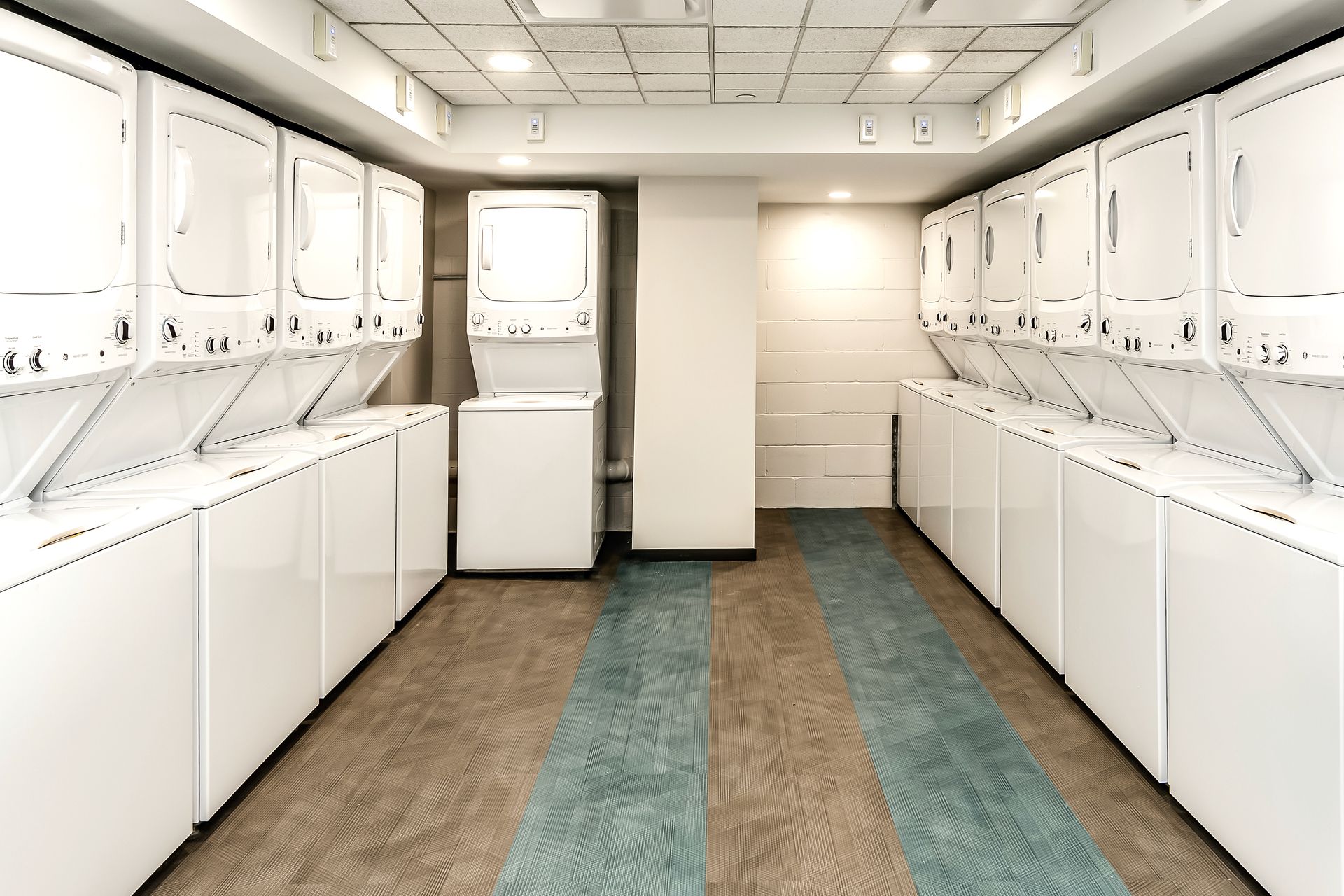 Bright laundromat with rows of white washers and dryers and a long carpeted aisle