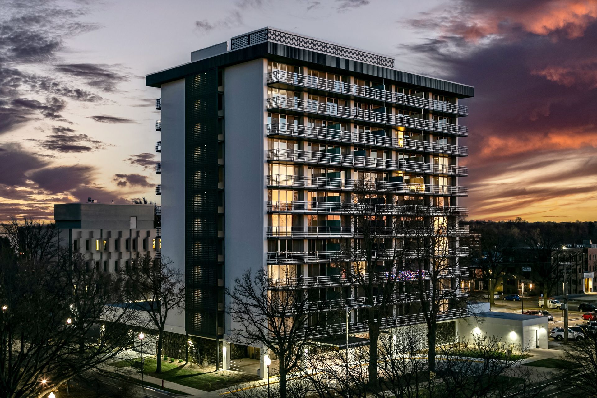 Modern high-rise building at dusk with lit balconies and sunset sky