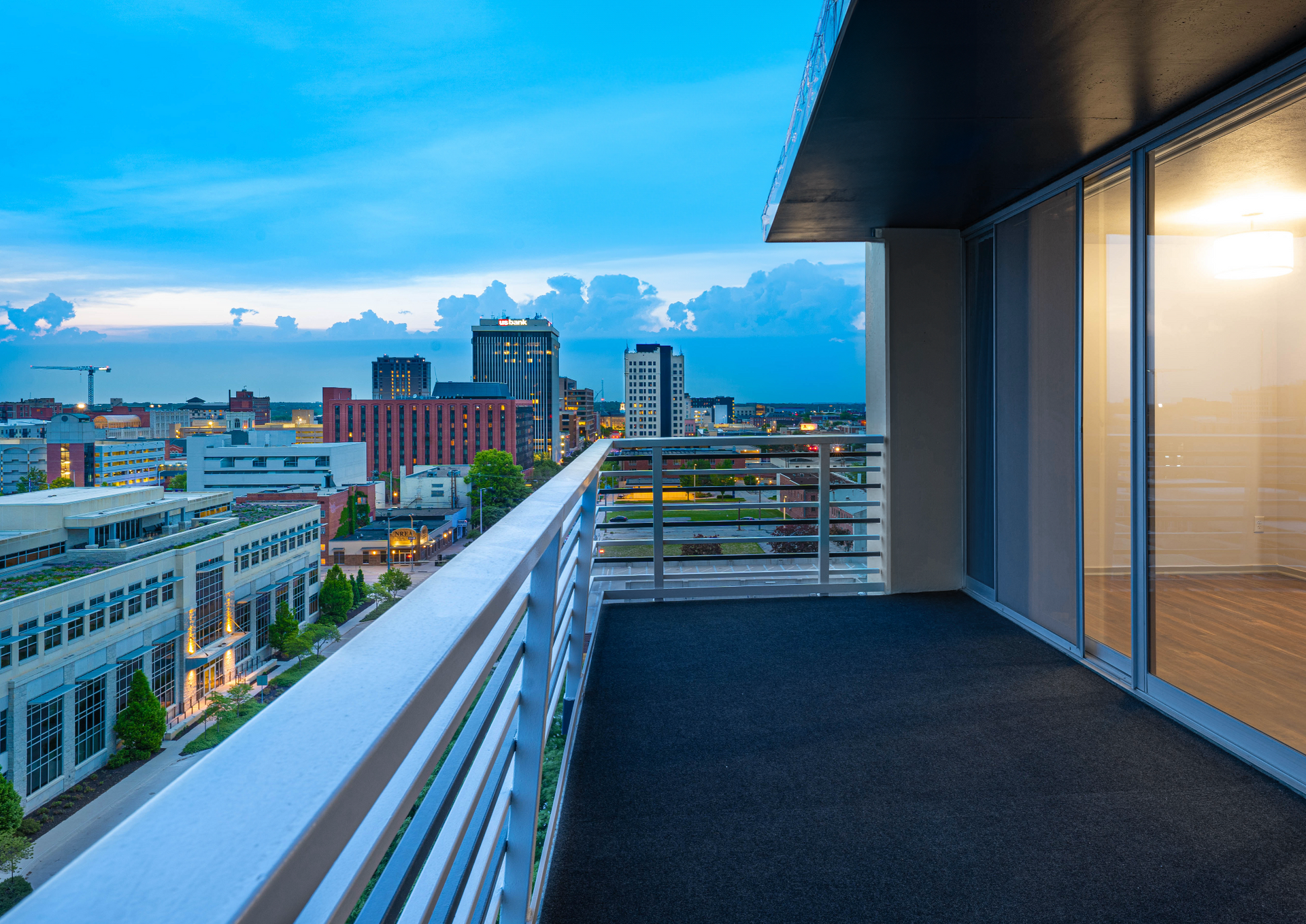 Balcony view of a city skyline at dusk, with white railings and lit apartment windows
