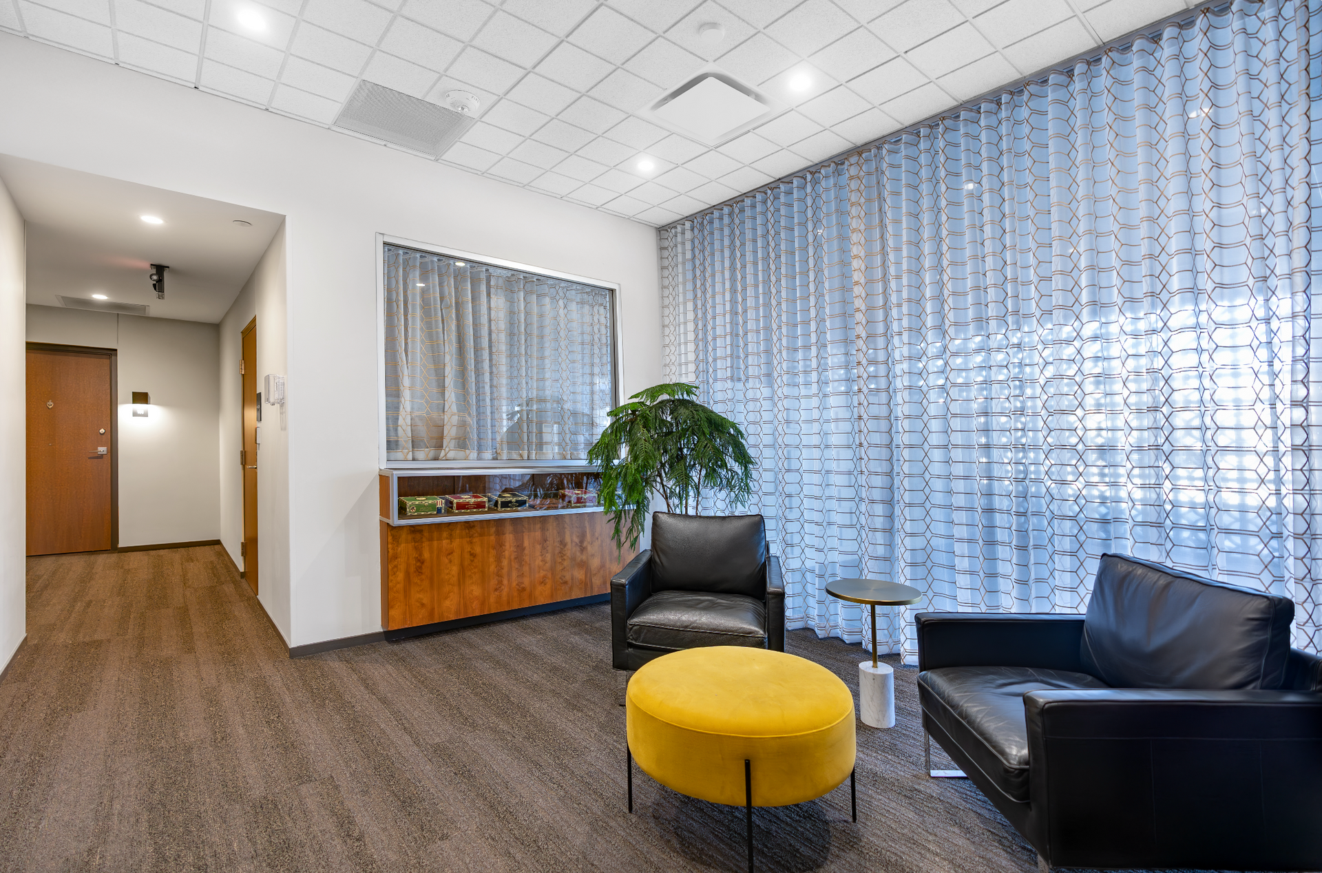 Modern waiting area with black chairs, yellow ottoman, wood desk, and sheer blue curtains