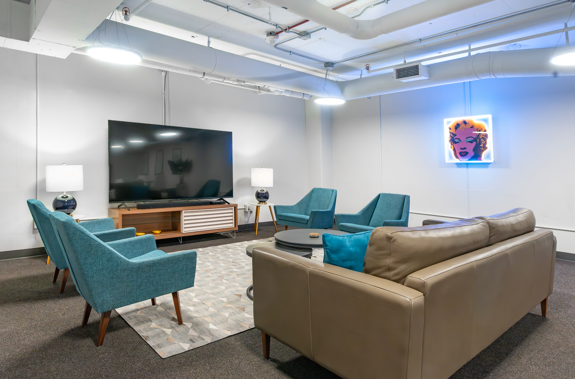 Modern living room with teal chairs, gray sofa, large TV, coffee table, and blue wall art