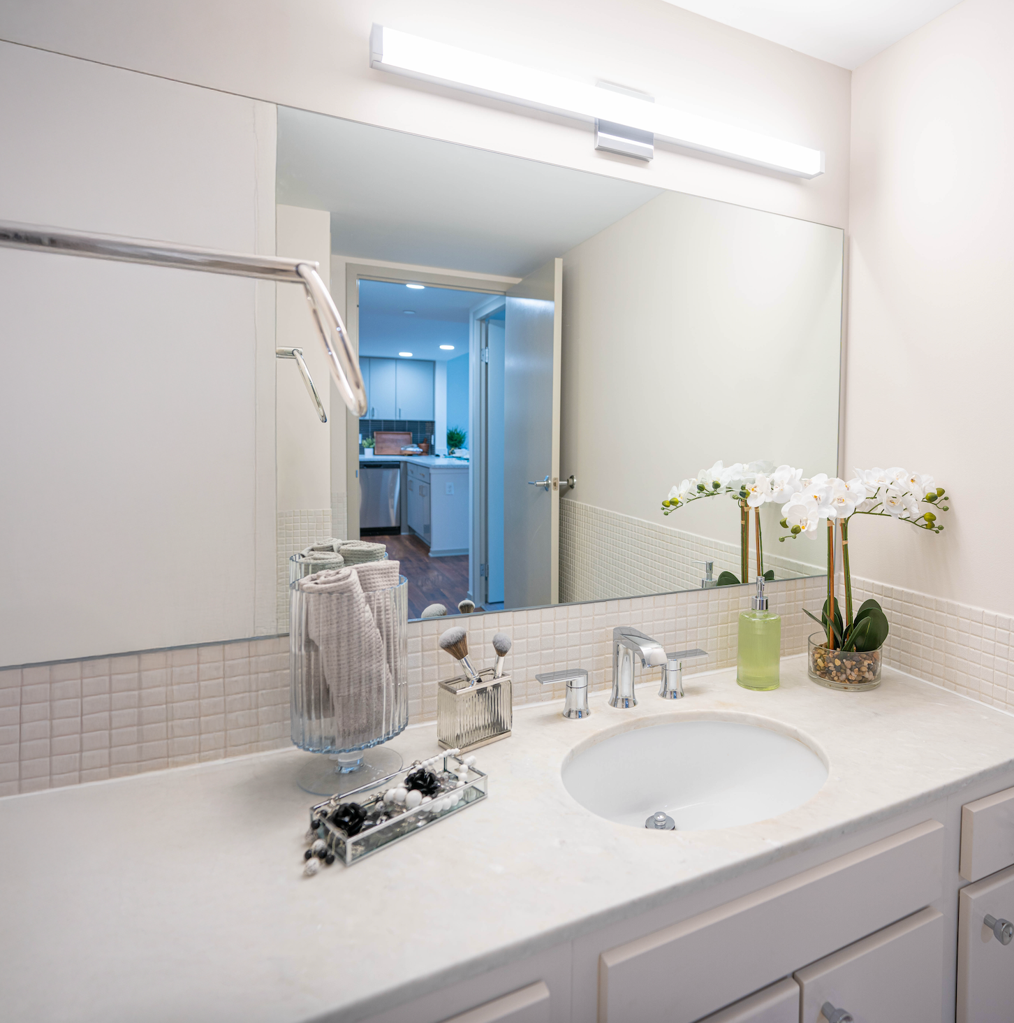 Bright white bathroom vanity with sink, mirror, toiletries, and orchid near an open doorway