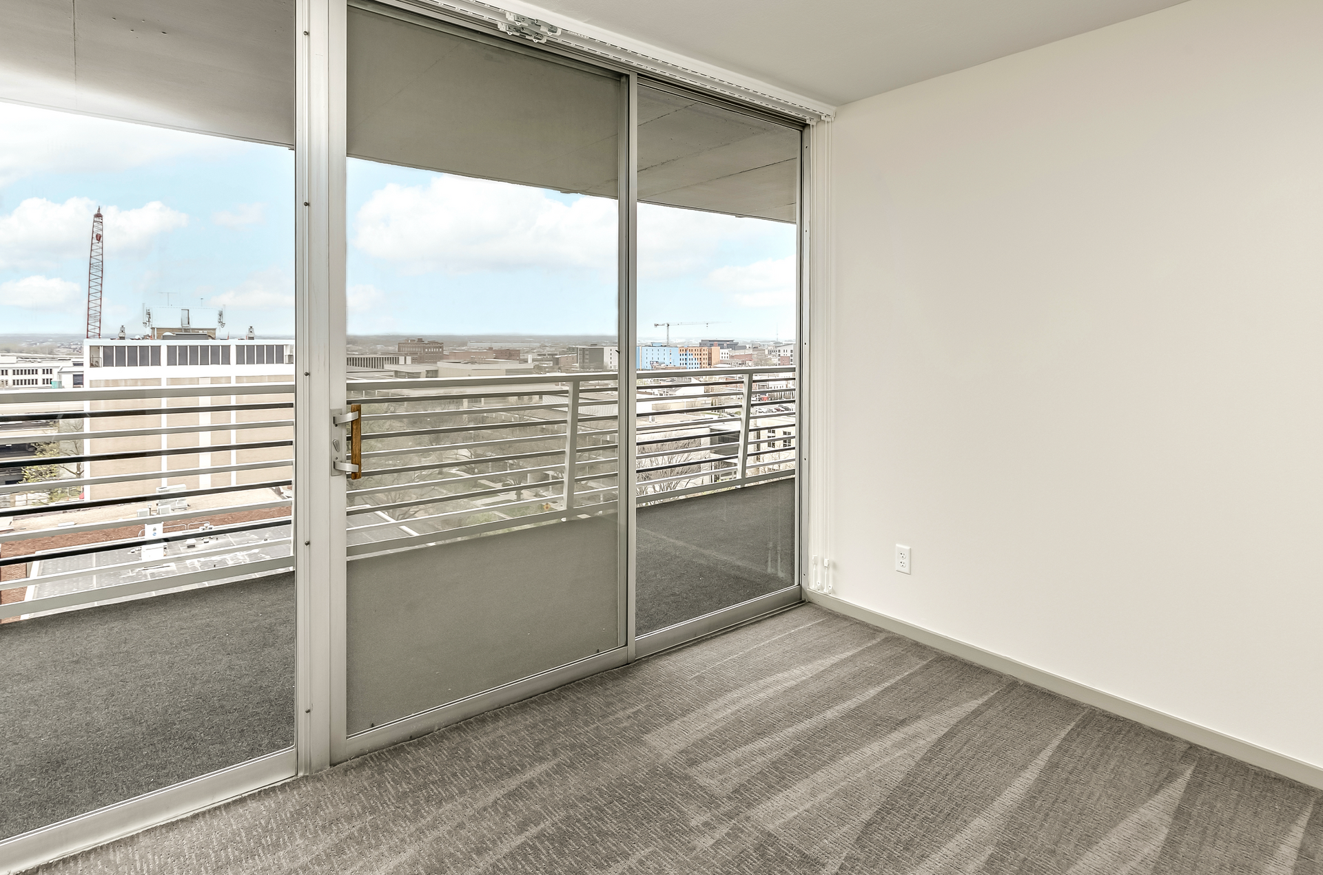 Empty apartment room with gray carpet and sliding glass doors opening to a city view.