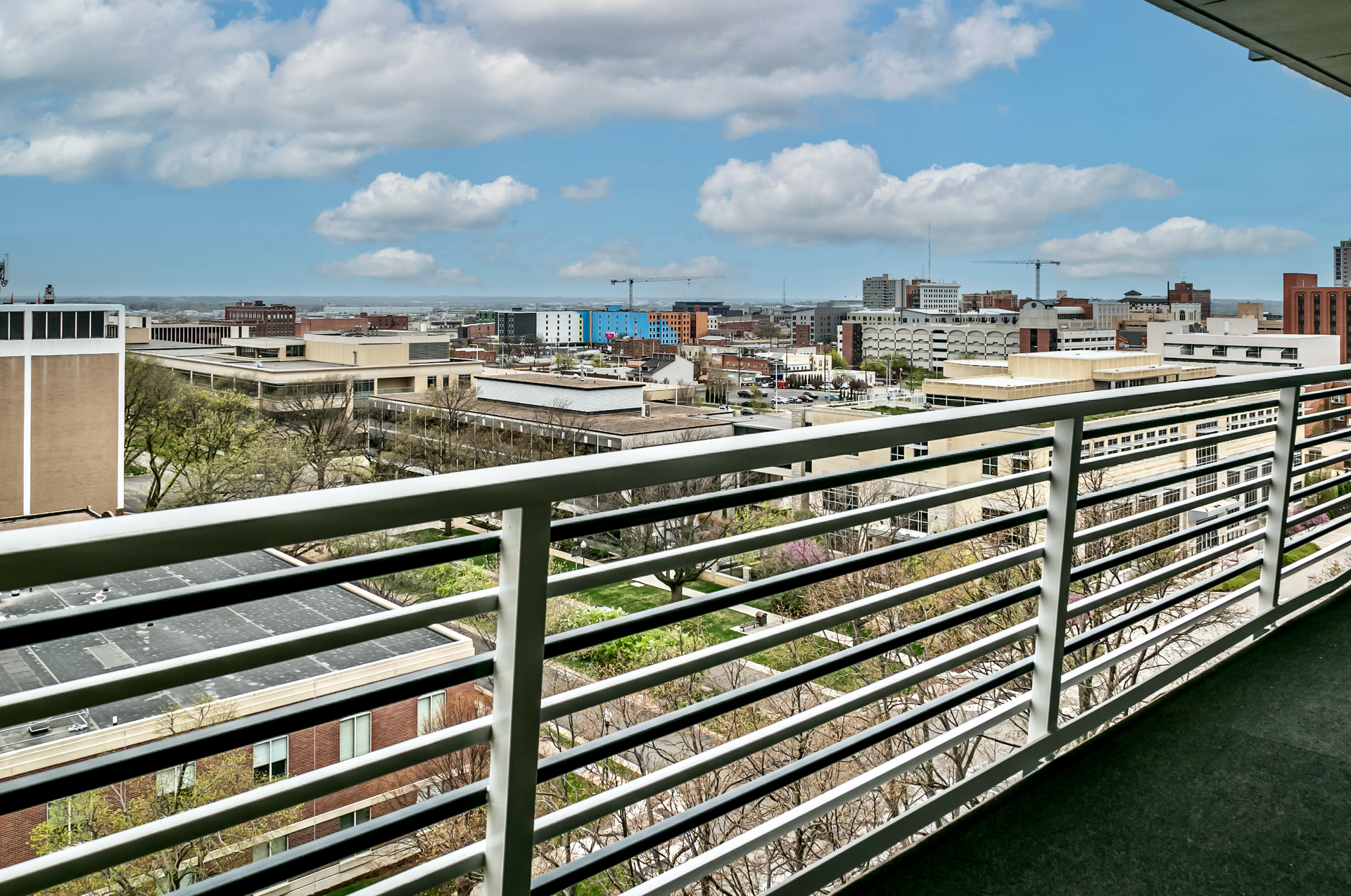 City skyline view from a balcony with metal railing under a blue sky with clouds