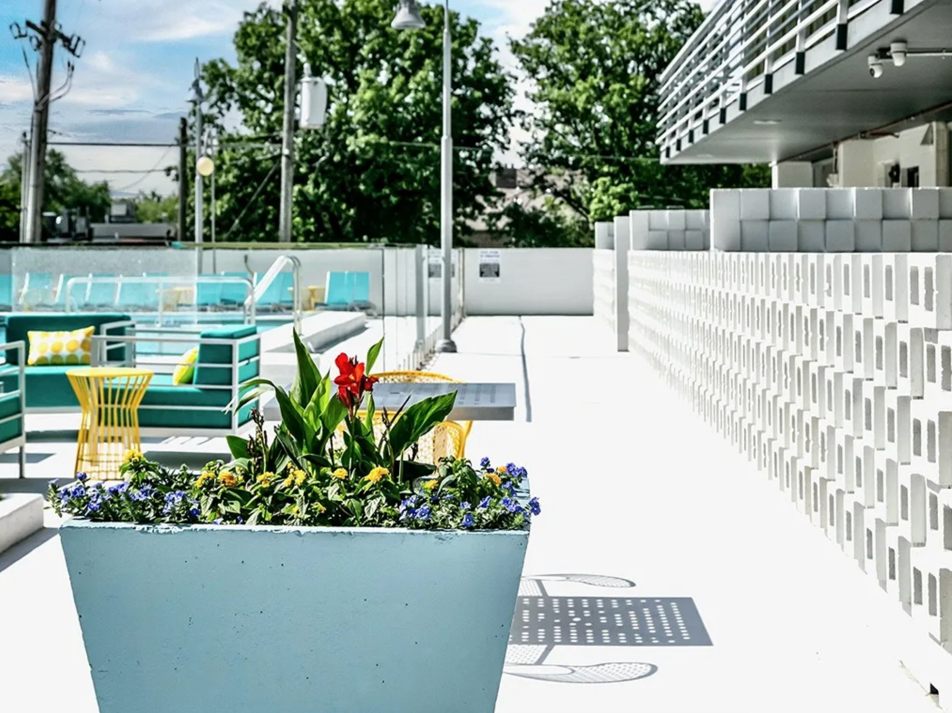 Bright patio with turquoise chairs, yellow table, potted flowers, and a white modern building wall
