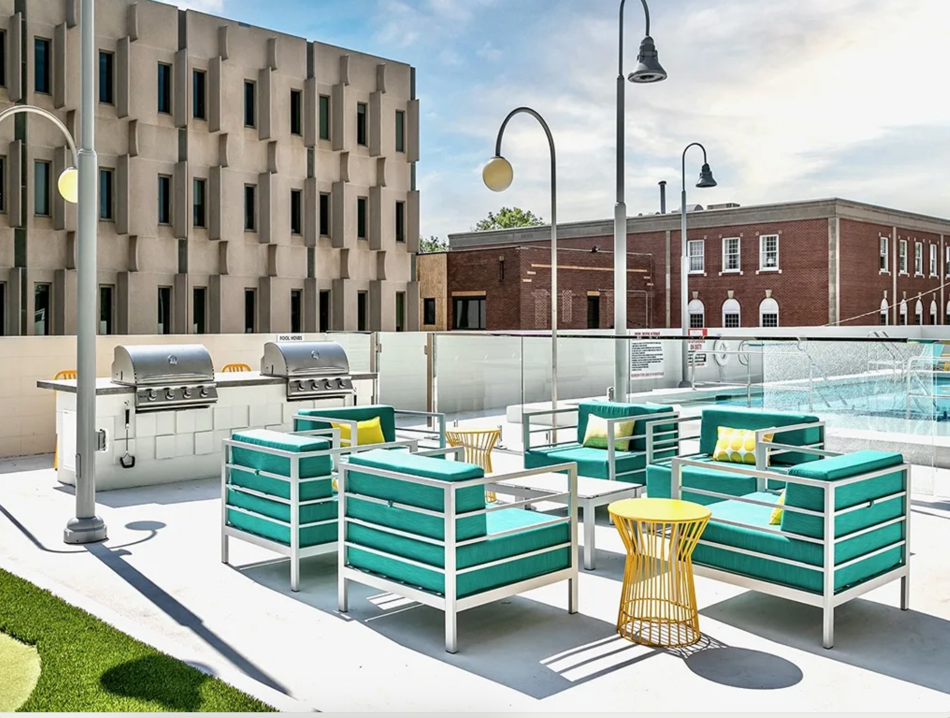 Rooftop patio with teal lounge seating, grill, and pool beside modern buildings