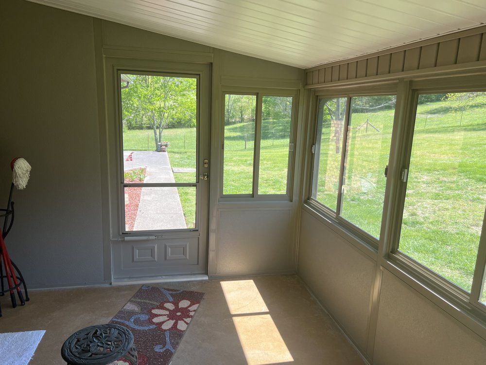 A screened in porch with a lot of windows and a door leading to a grassy field.