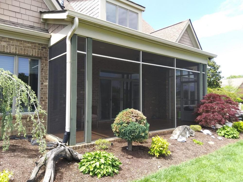 A screened in porch is being built on the side of a brick house.