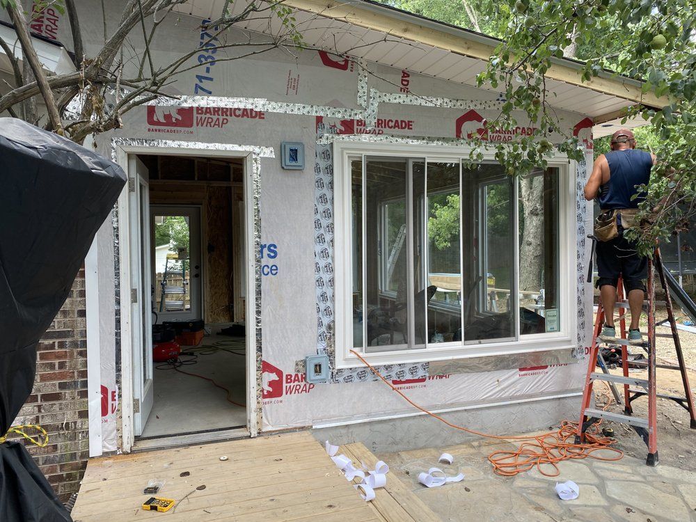 A man is standing on a ladder working on a window on the side of a house.