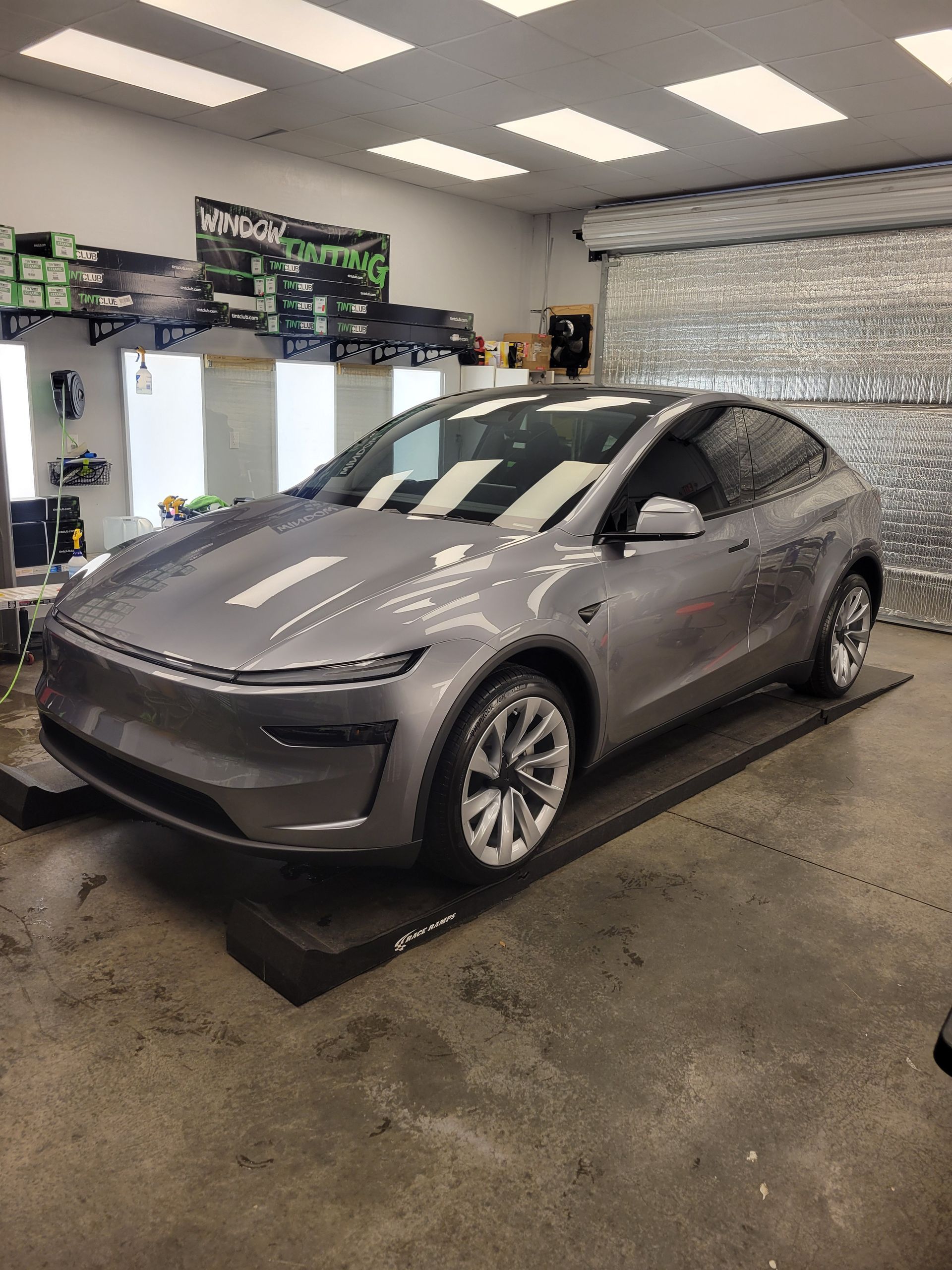 Gray Tesla sedan in a garage, viewed from the front-left side.
