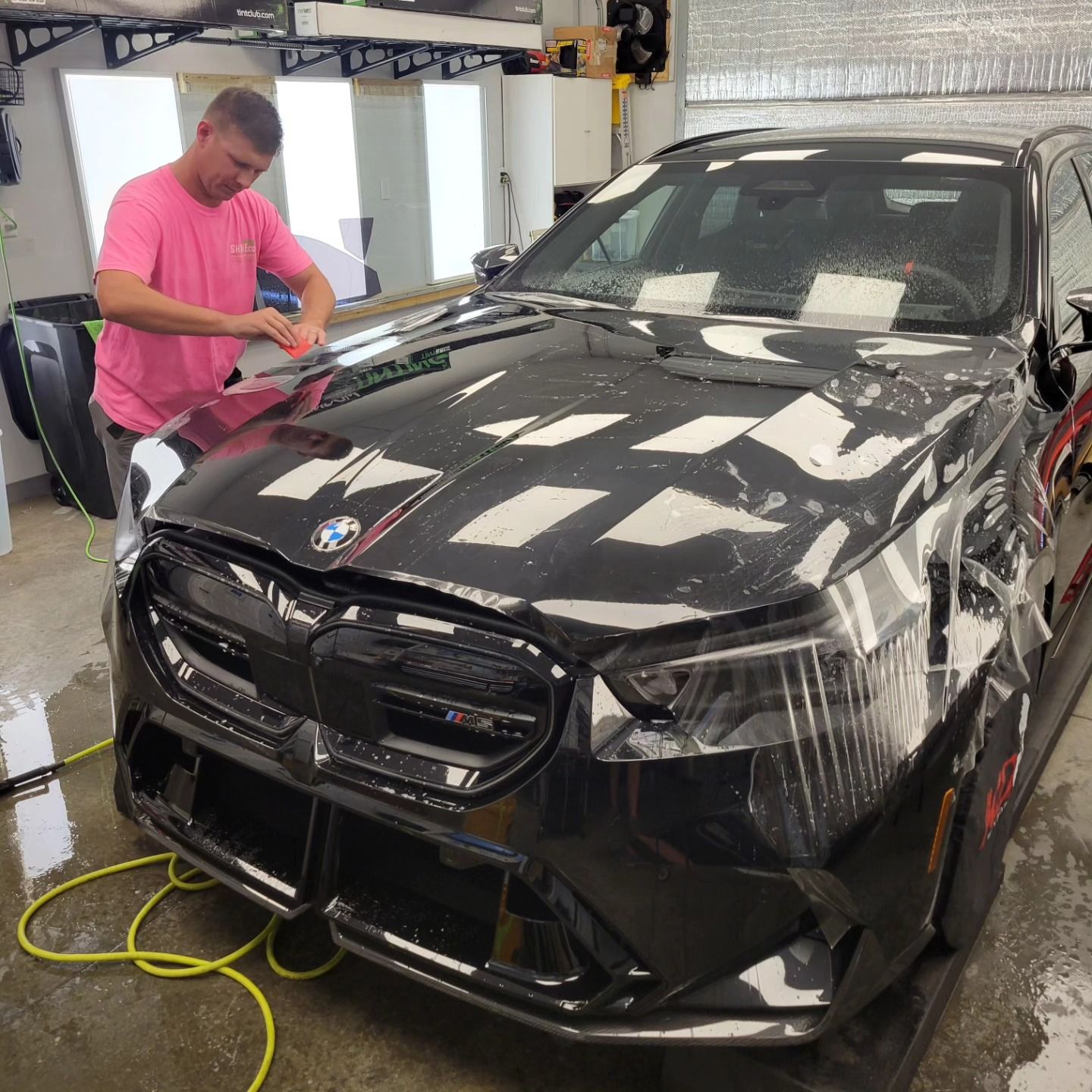 Man polishing a black BMW sedan in a garage, with water and detailing equipment nearby