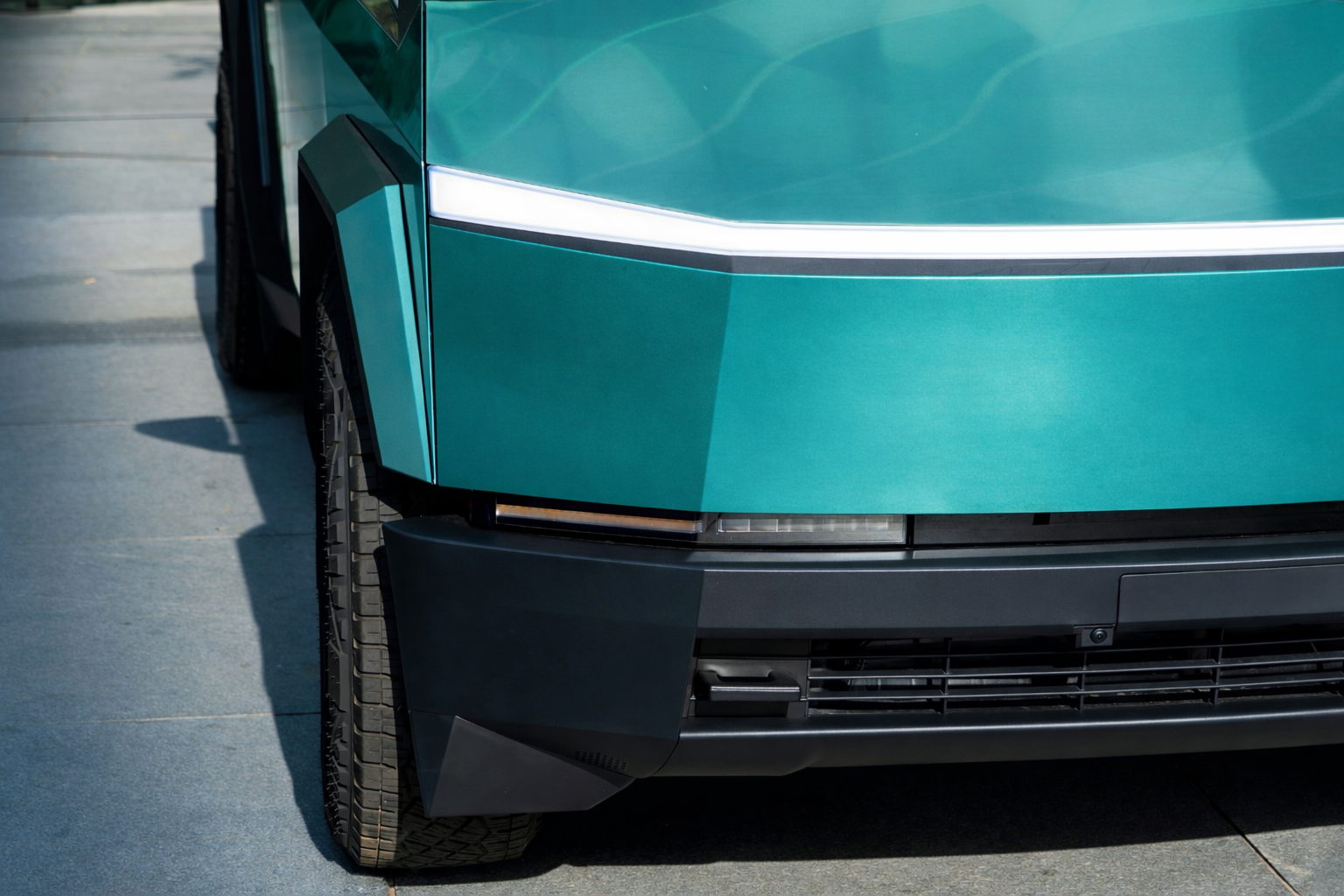 Close-up of the front-left corner of a teal car parked on a driveway.
