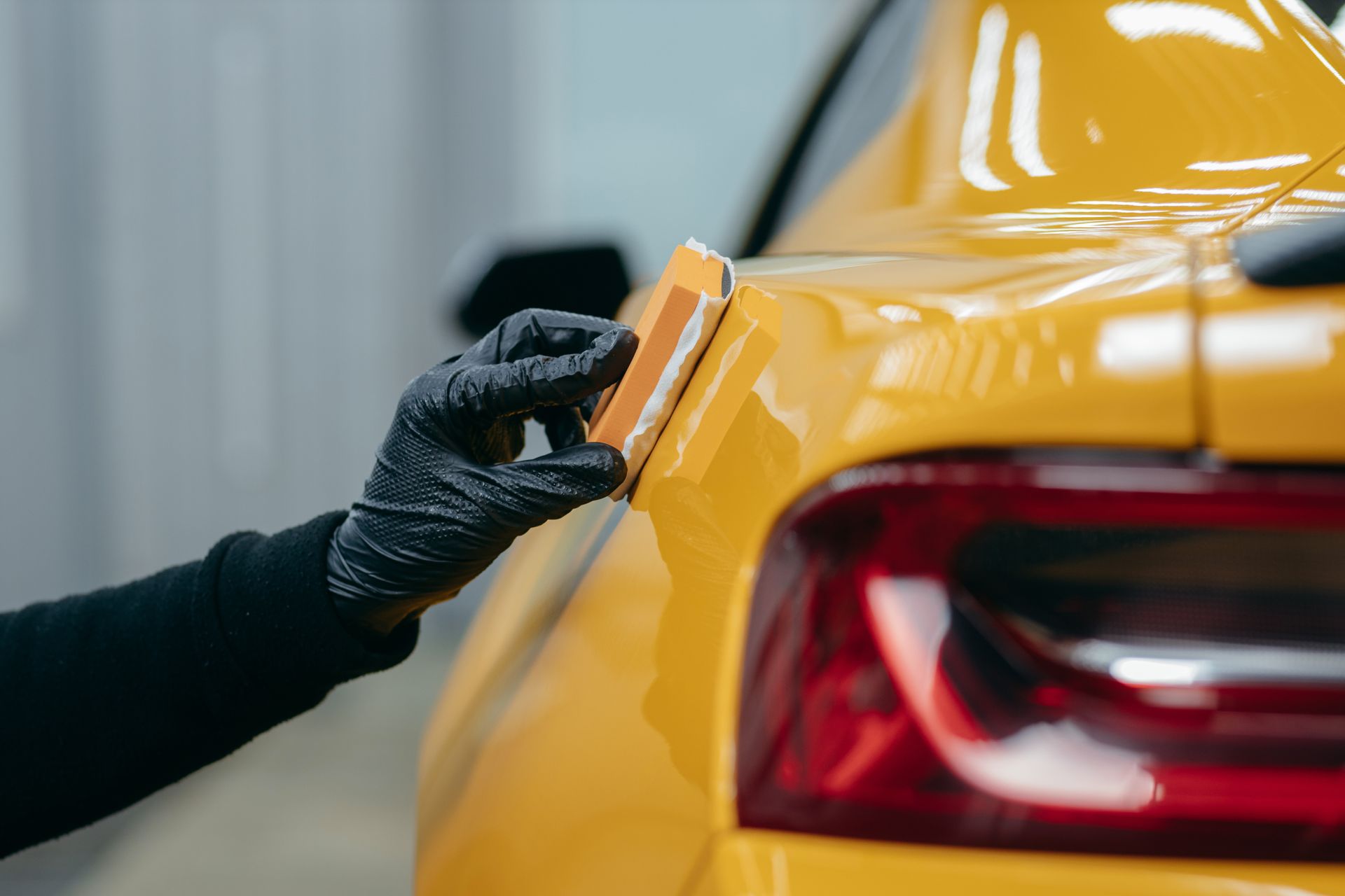 Gloved hand polishing the rear of a yellow car with a cloth