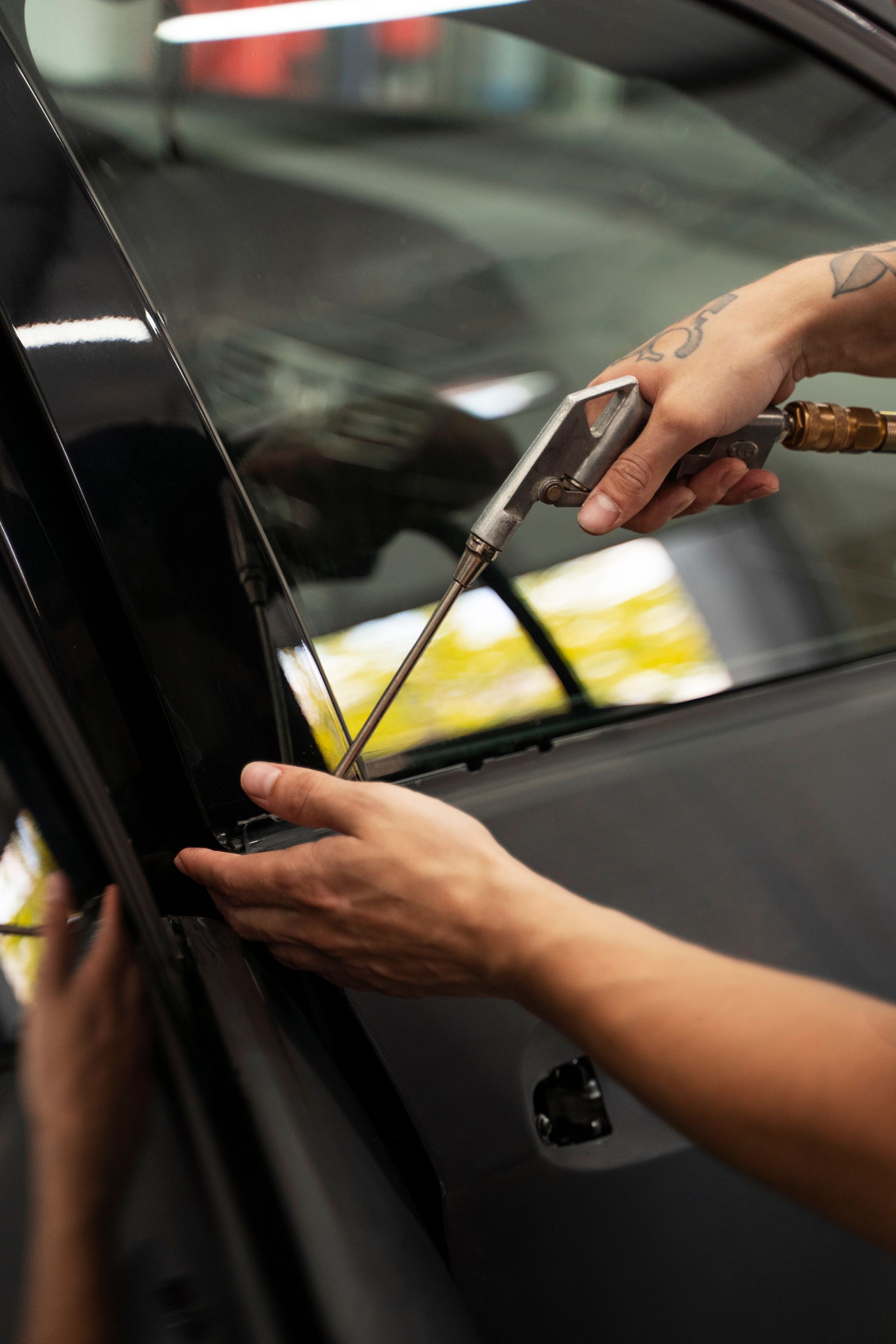 A person applies yellow masking tape along a car window with a tool during auto detailing.