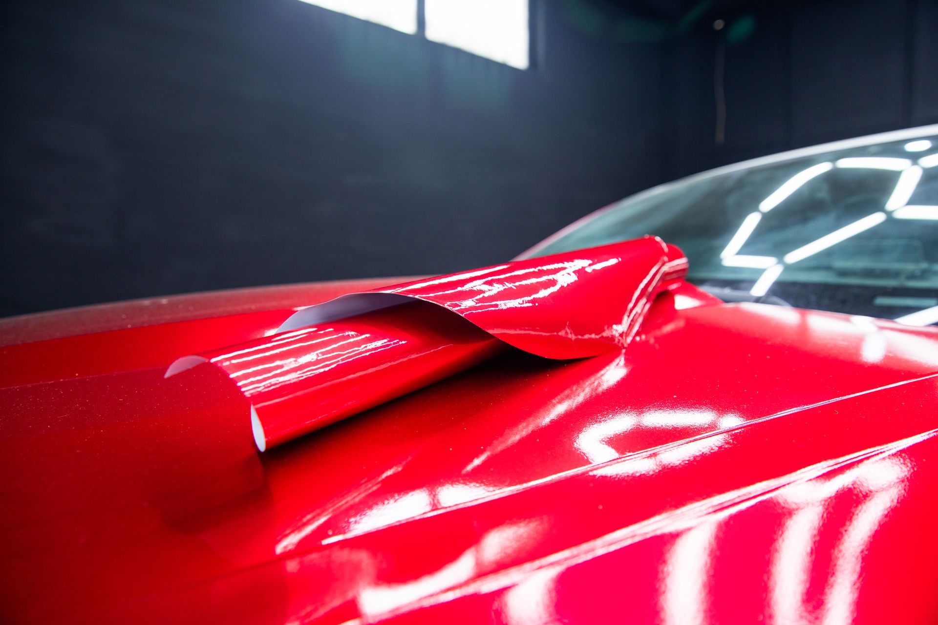 Close-up of a glossy red sports car hood with a raised scoop in a dim garage