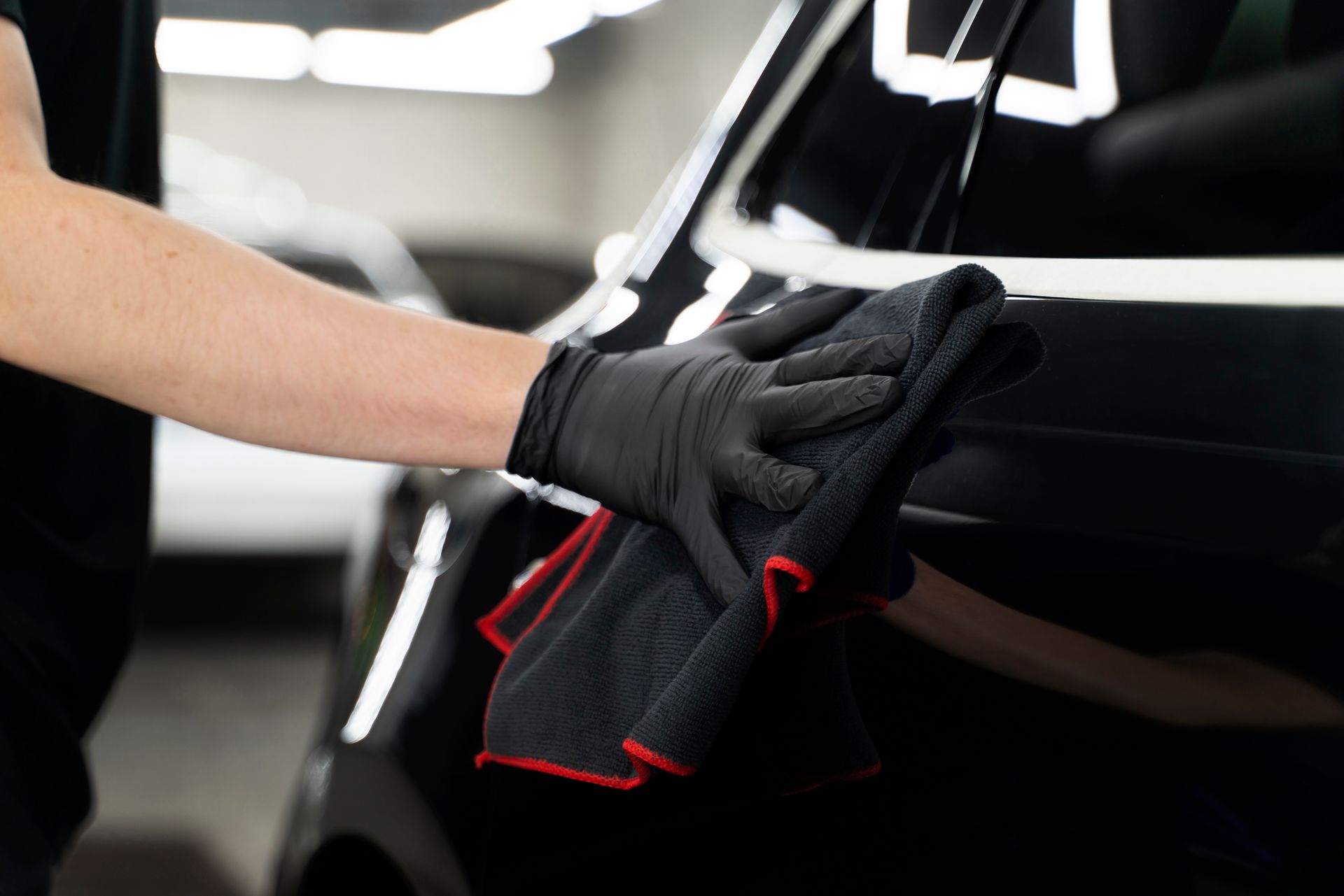 Person wearing black gloves wiping down a black car with a microfiber towel.