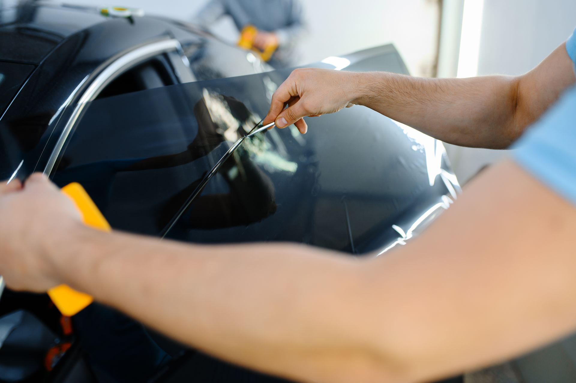 Hands polishing a black car windshield with a cloth in a garage