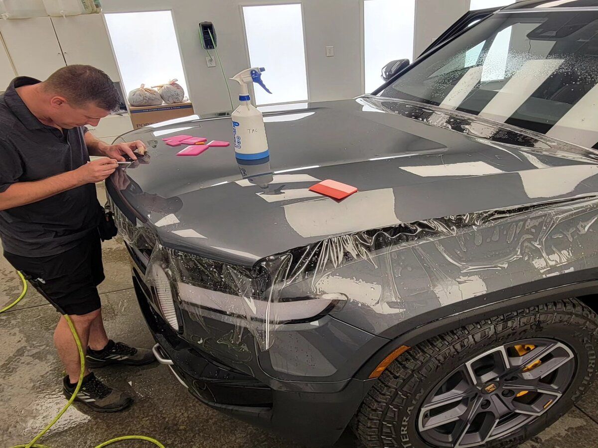 Man polishing a gray SUV in a workshop, with masking tape and tools on the hood.
