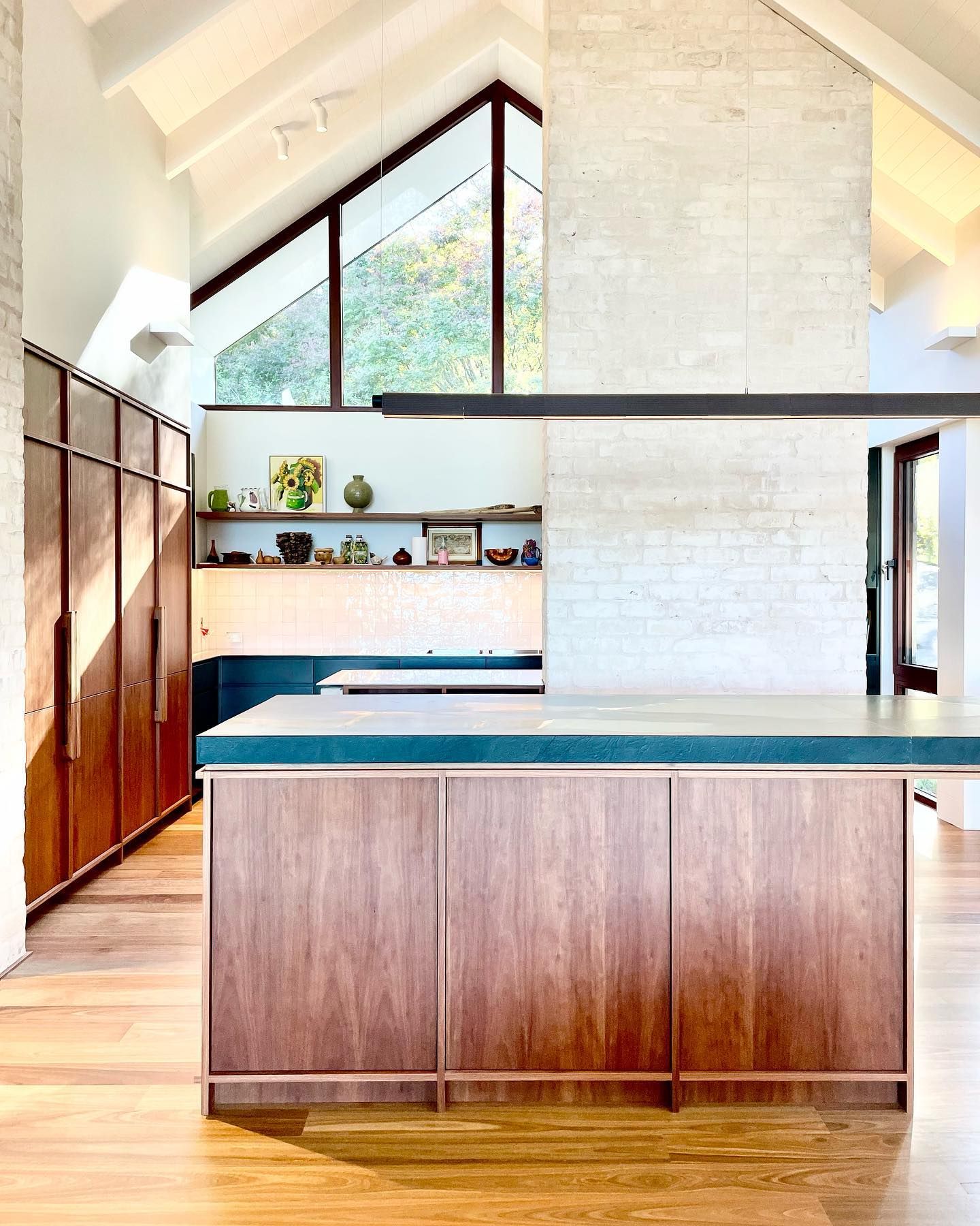 Modern kitchen with wood cabinetry, white brick wall, and sloped ceiling with triangle window — BSpoke Cabinet Making & Joinery in Unanderra, NSW