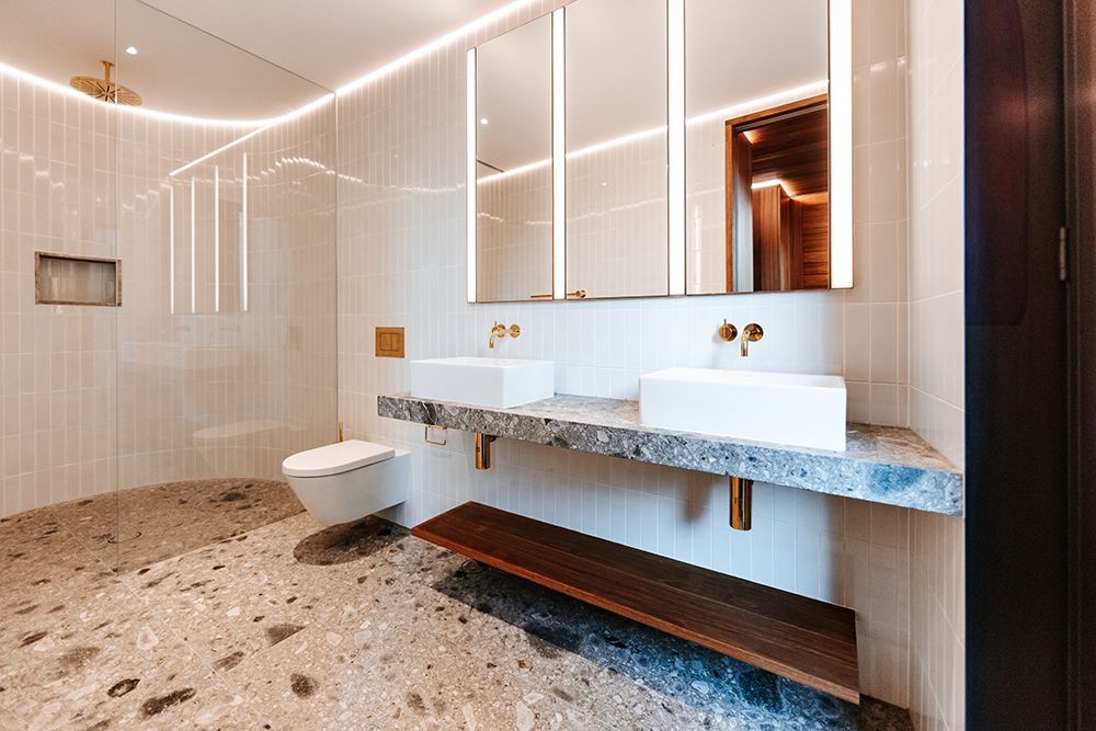 Modern bathroom with white and gold fixtures, terrazzo floor, floating vanity with two sinks, and a walk-in shower — BSpoke Cabinet Making & Joinery in Unanderra, NSW