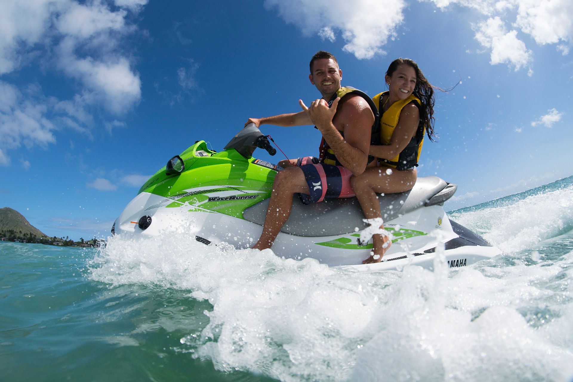 Two people riding a jet ski through blue water under a sunny sky