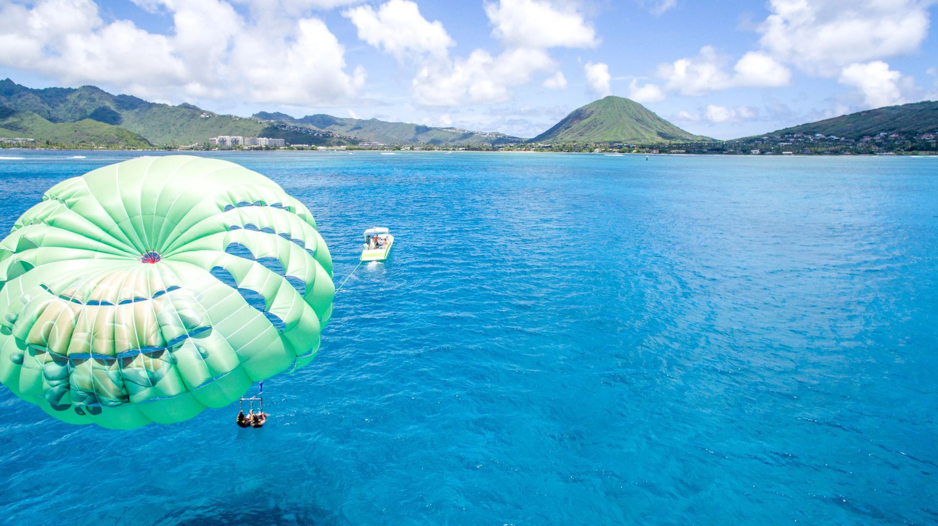 Bright green parasail over vivid blue ocean near a tropical shoreline and distant hills