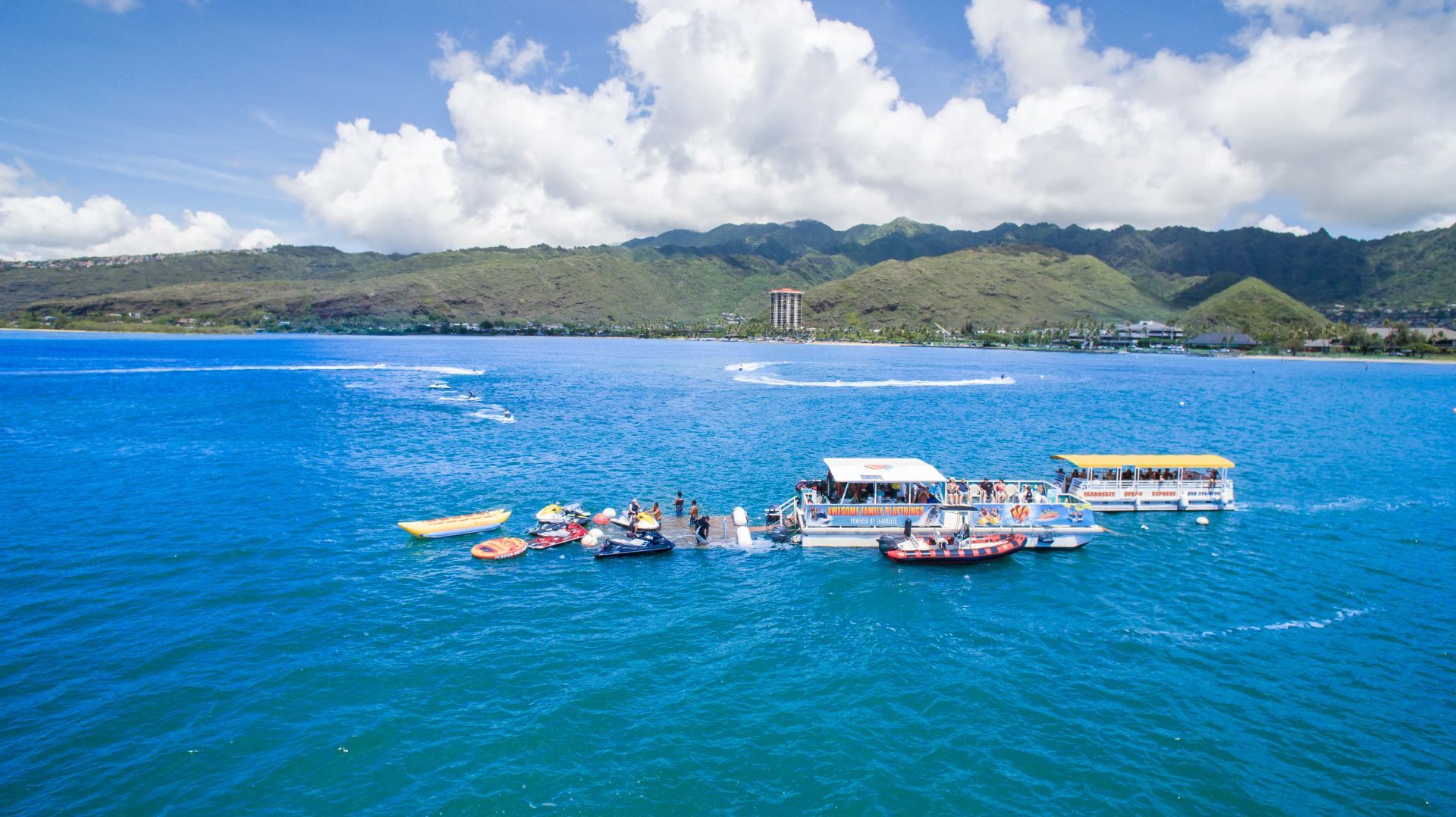 Floating rafts on bright blue water with a green coastline and mountains in the distance