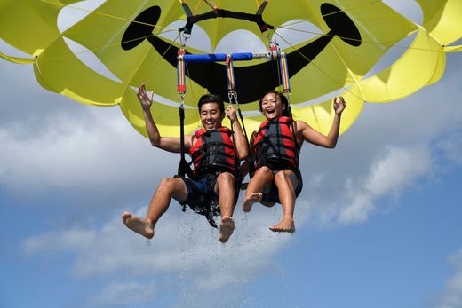 Two people parasailing under a yellow canopy against a blue sky