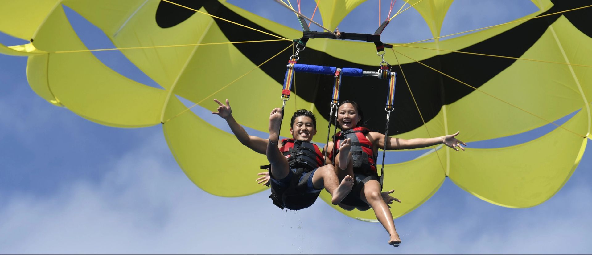 Two people parasailing under yellow canopies against a blue sky