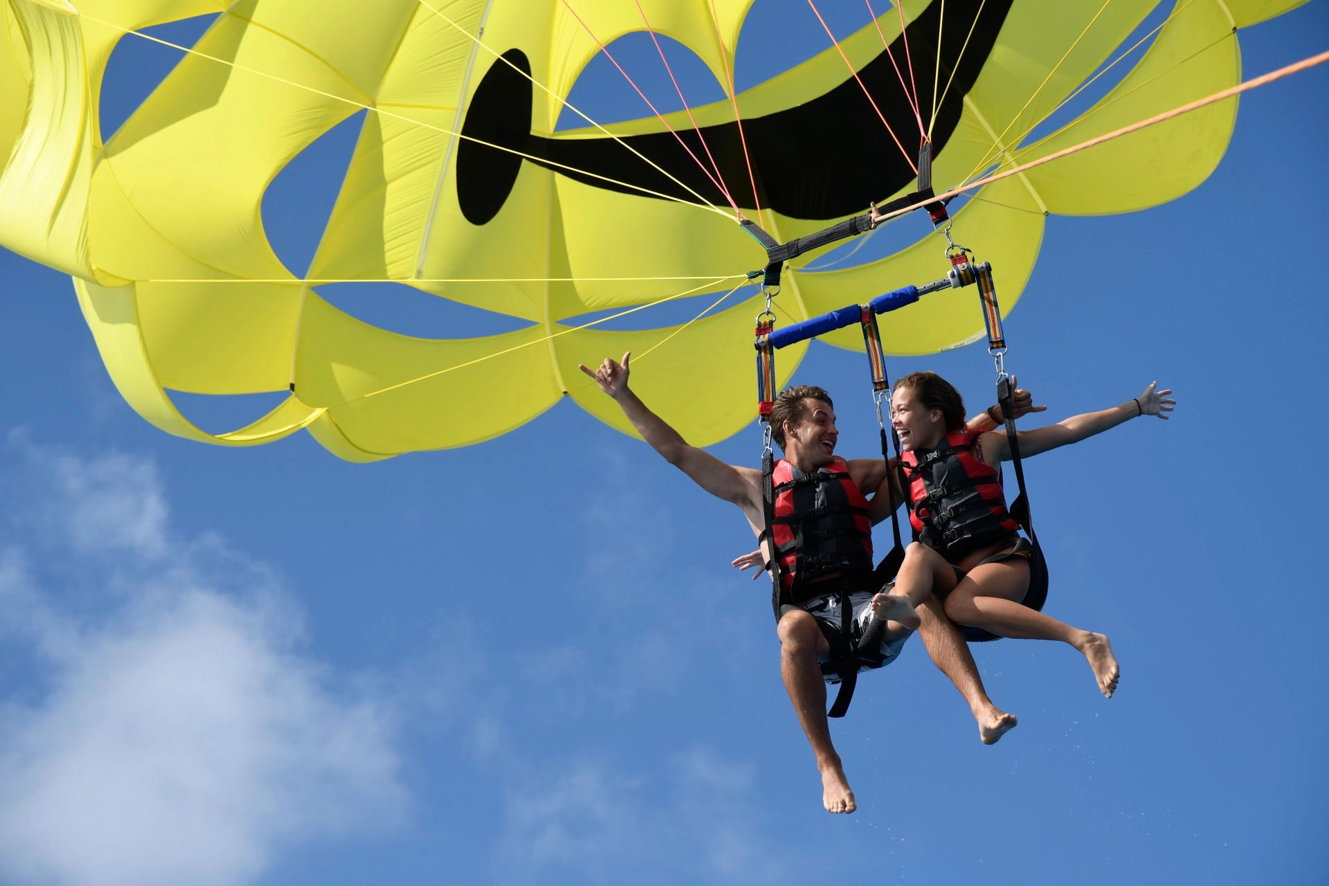 Two people tandem parasailing under a bright yellow canopy against a blue sky